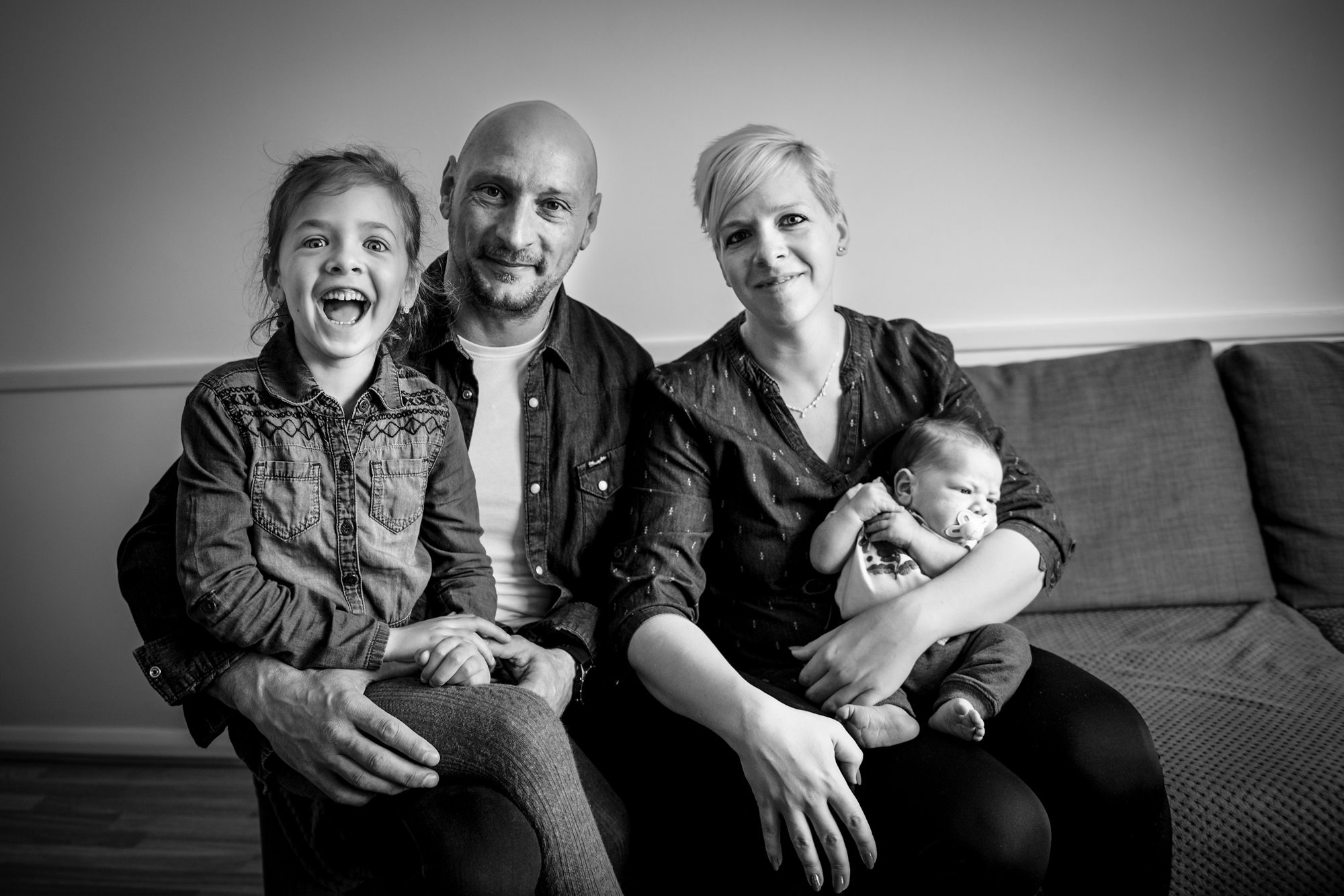 Family of four sits together on the sofa during an at-home newborn session.