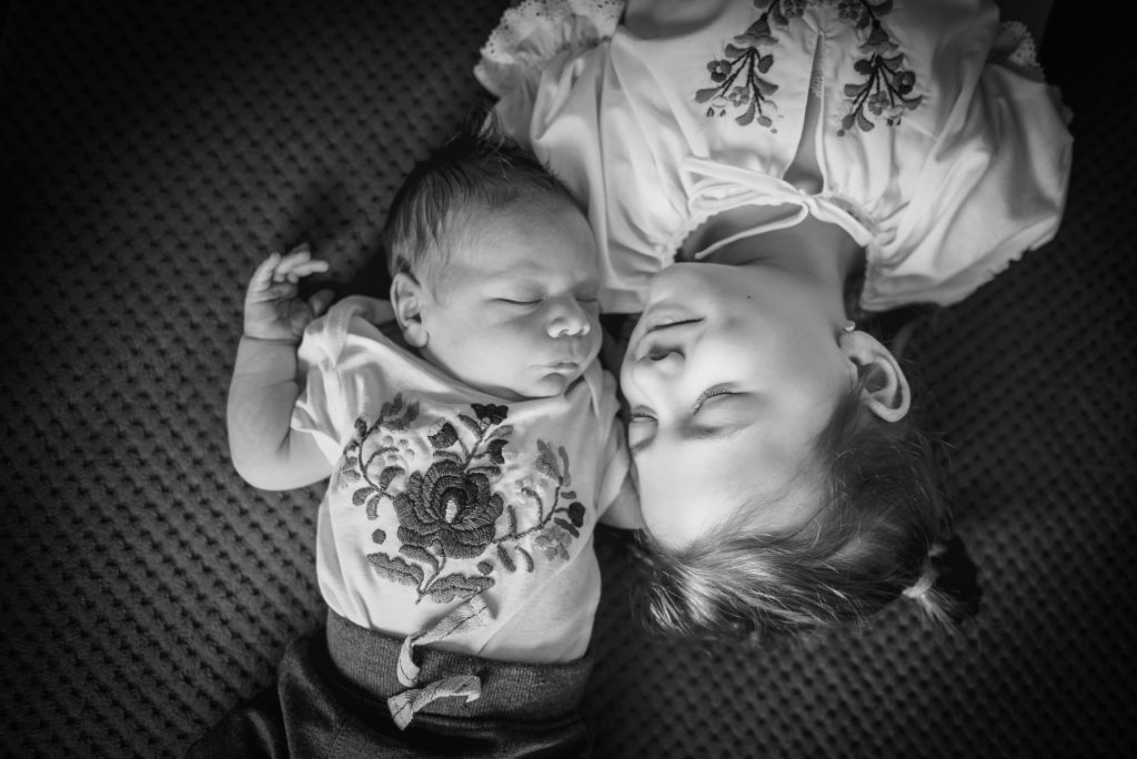 Older sister lies beside the newborn in a sibling portrait.