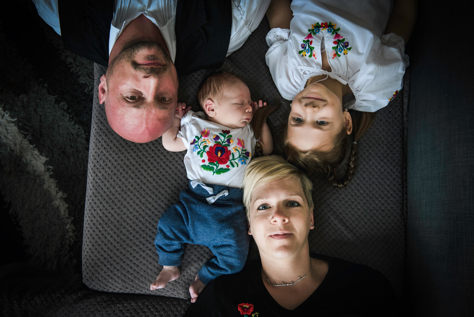 Family of four lies together on a sofa with the newborn sleeping between them.