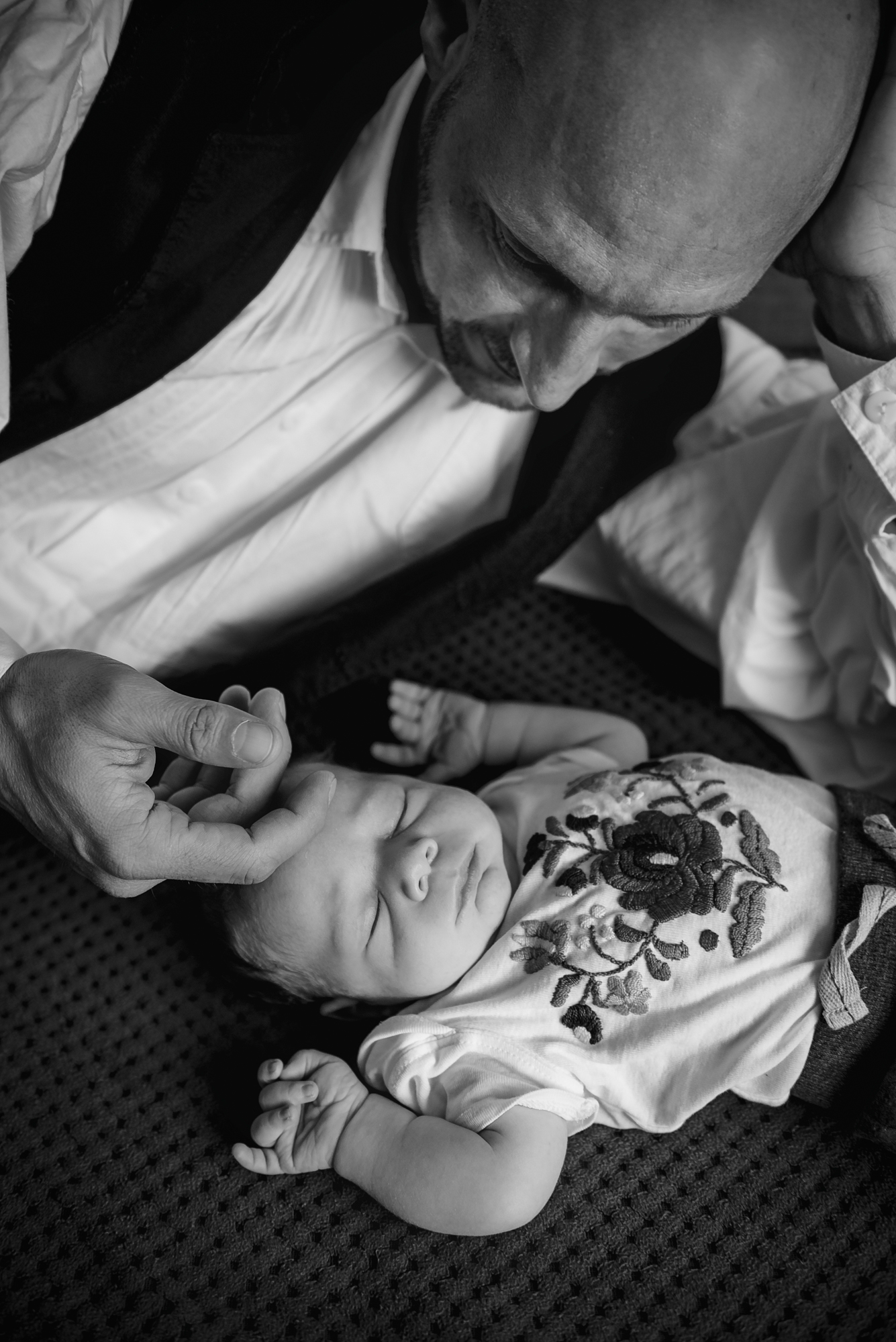Dad watching his sleeping newborn on a textured blanket.