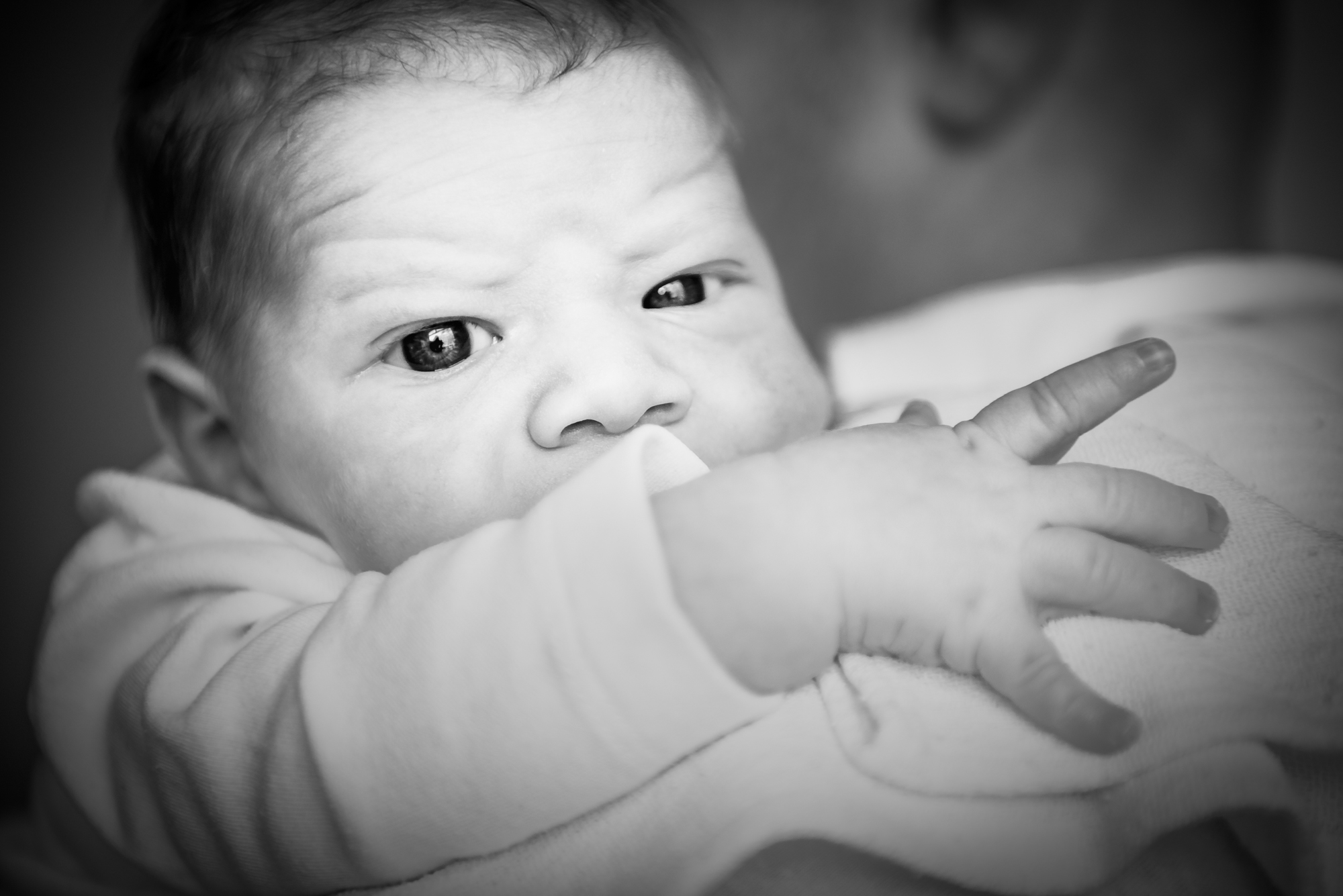 Close-up of a newborn gazing over an adult’s shoulder.