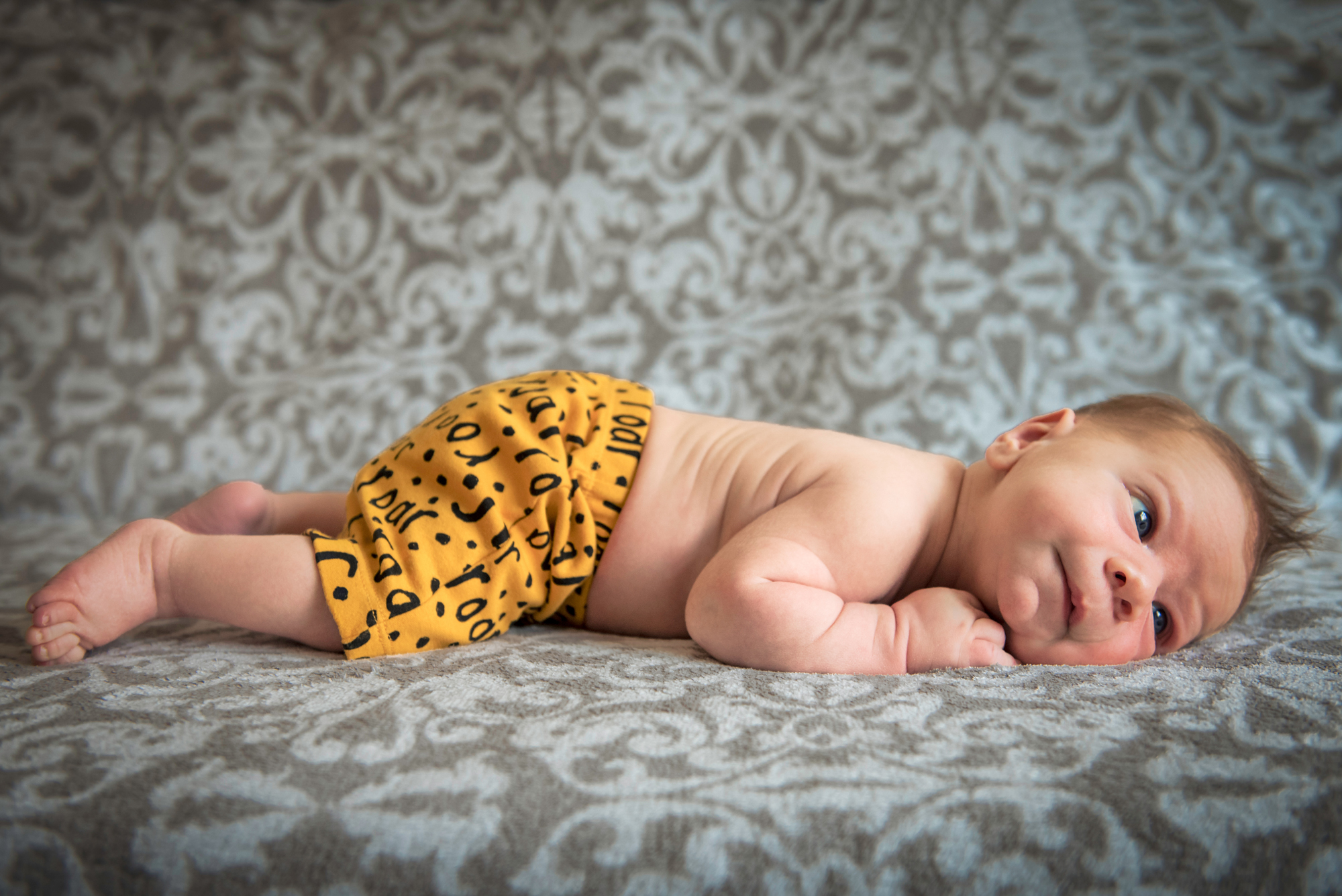 Newborn lies on a patterned blanket wearing mustard shorts during an at-home session.