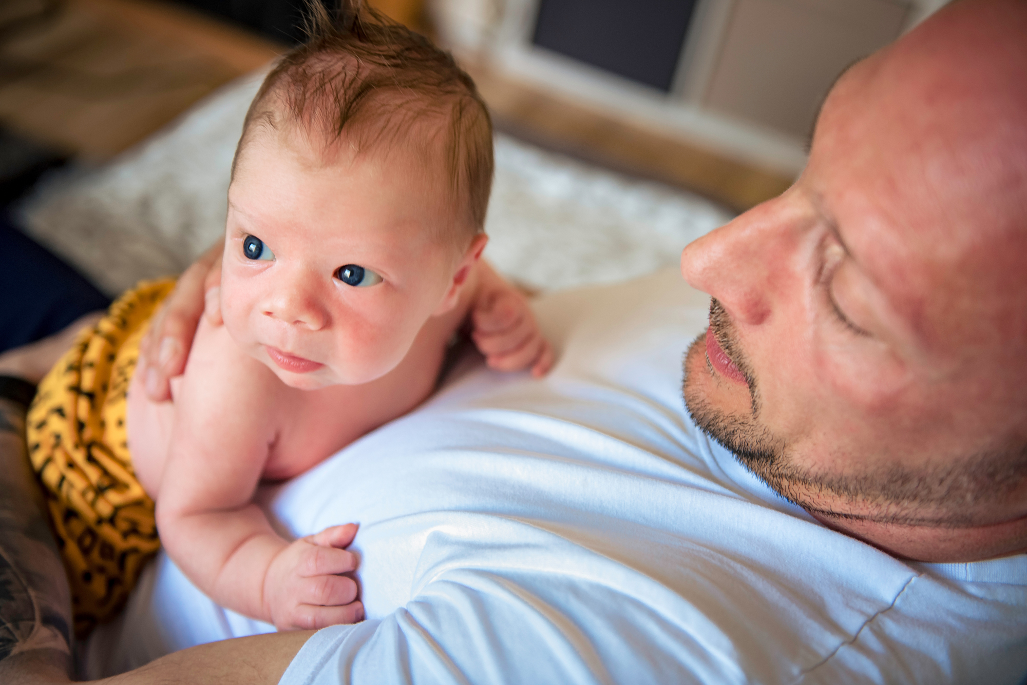 Blue-eyed newborn lies on dad’s chest during a relaxed lifestyle newborn session.