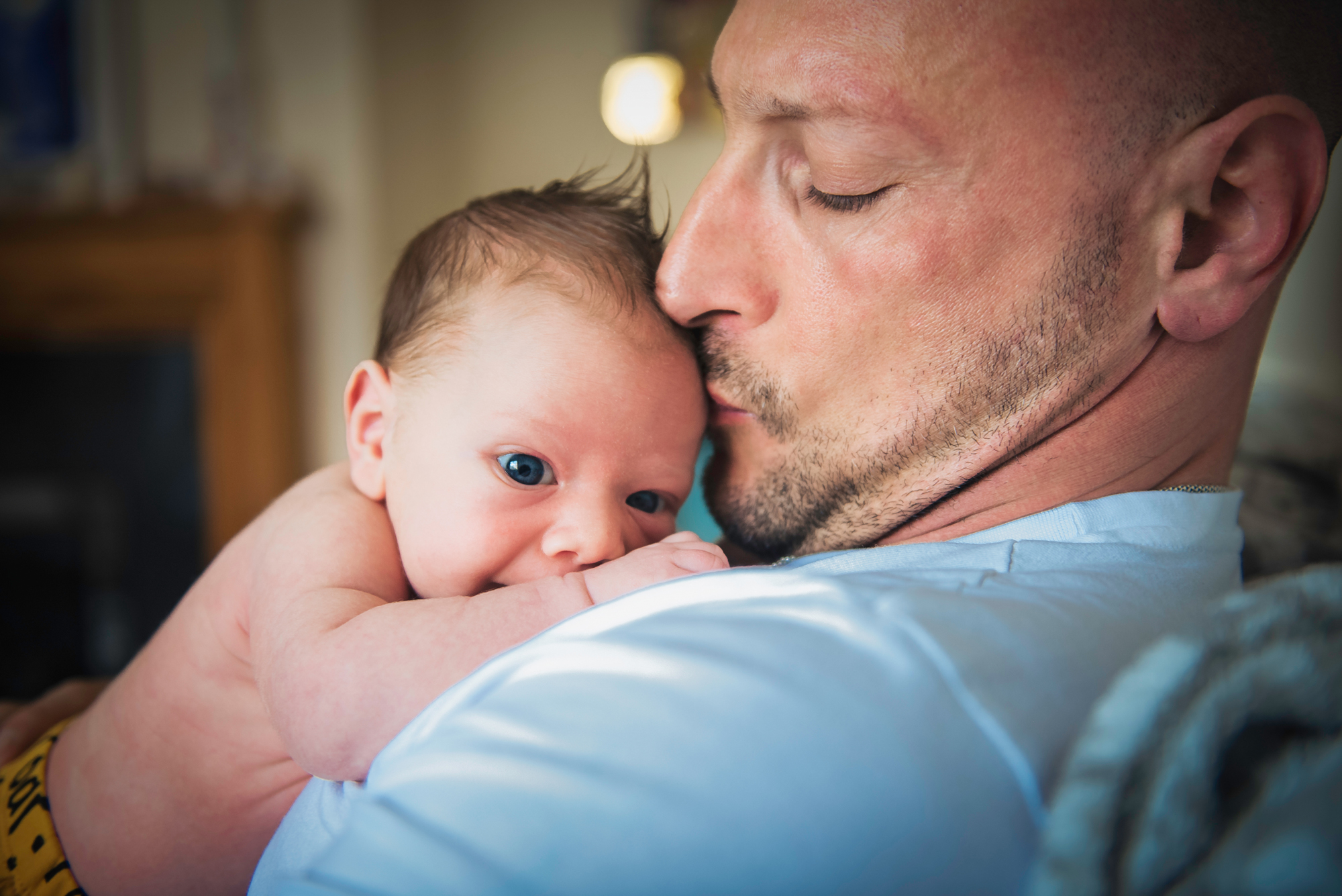 Dad kisses newborn’s forehead while the baby looks calmly toward the camera.