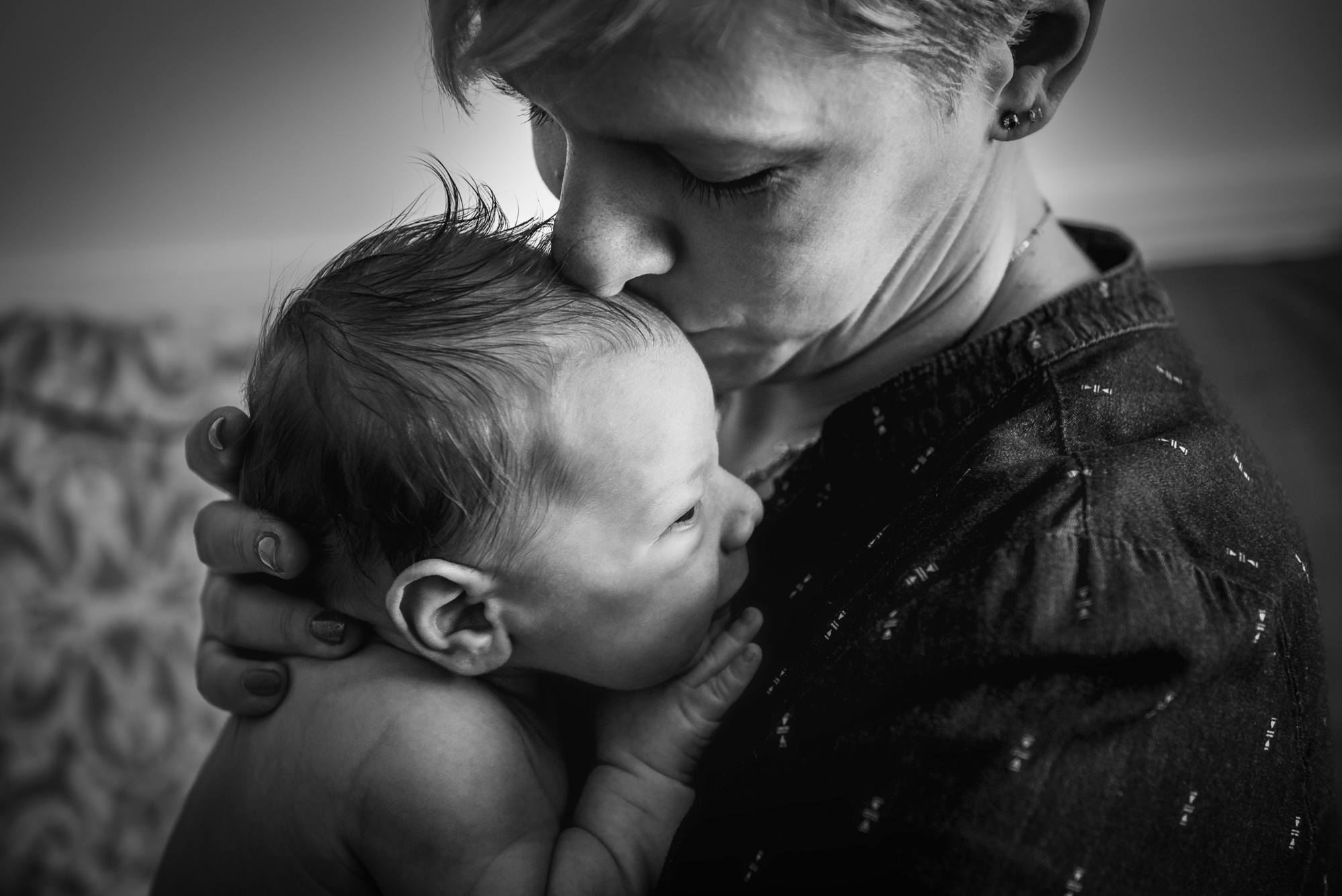 Mum kisses newborn’s head while holding the baby close.