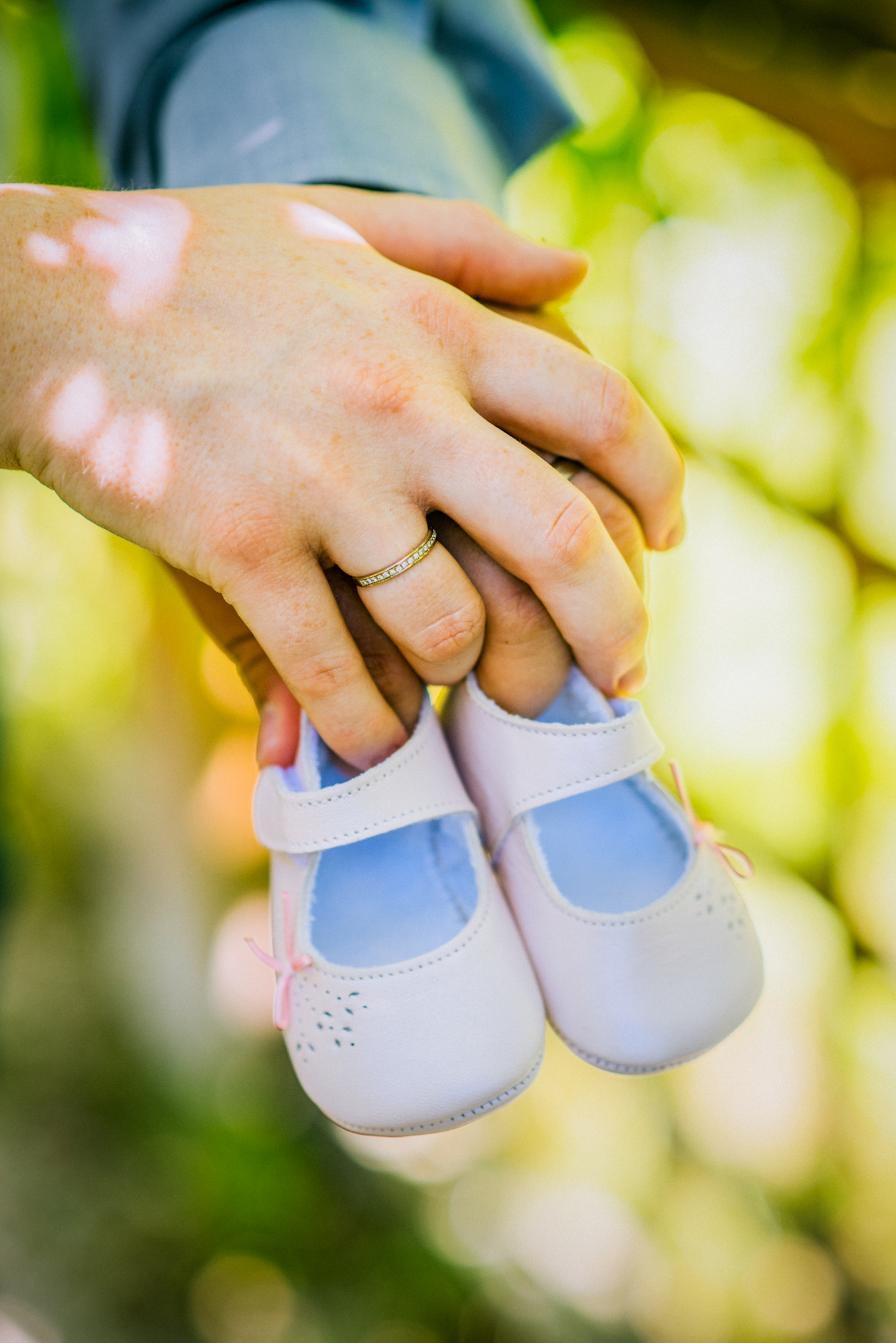 Close-up of hands holding baby shoes with engagement ring visible in natural light.