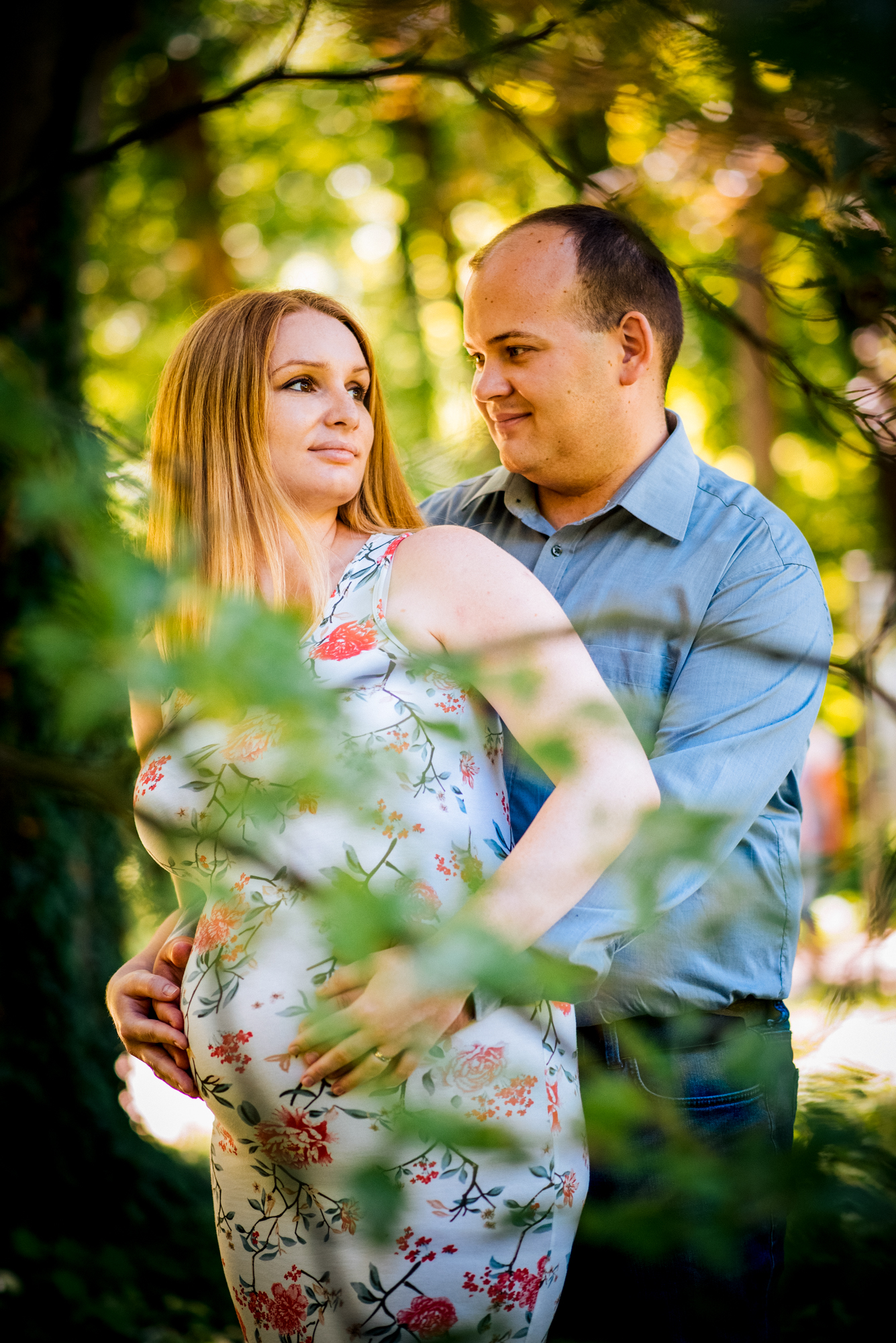 Close portrait of couple embracing outdoors, framed by soft greenery and golden light.