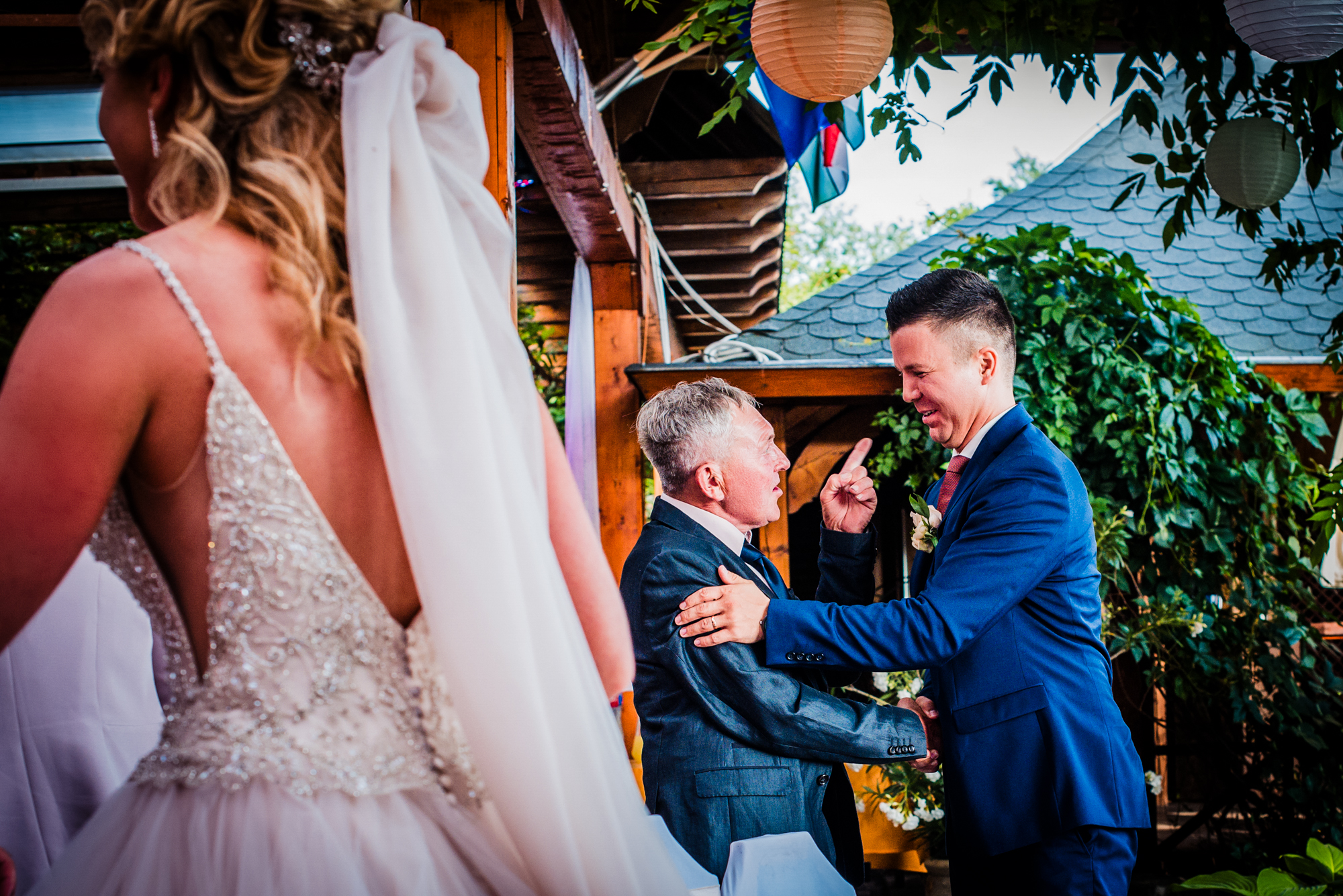Groom greeting older guest with handshake during wedding reception, bride in foreground.