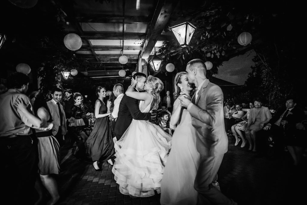 Couple kissing on the dance floor surrounded by dancing guests at a wedding reception, documentary wedding photography in black and white.