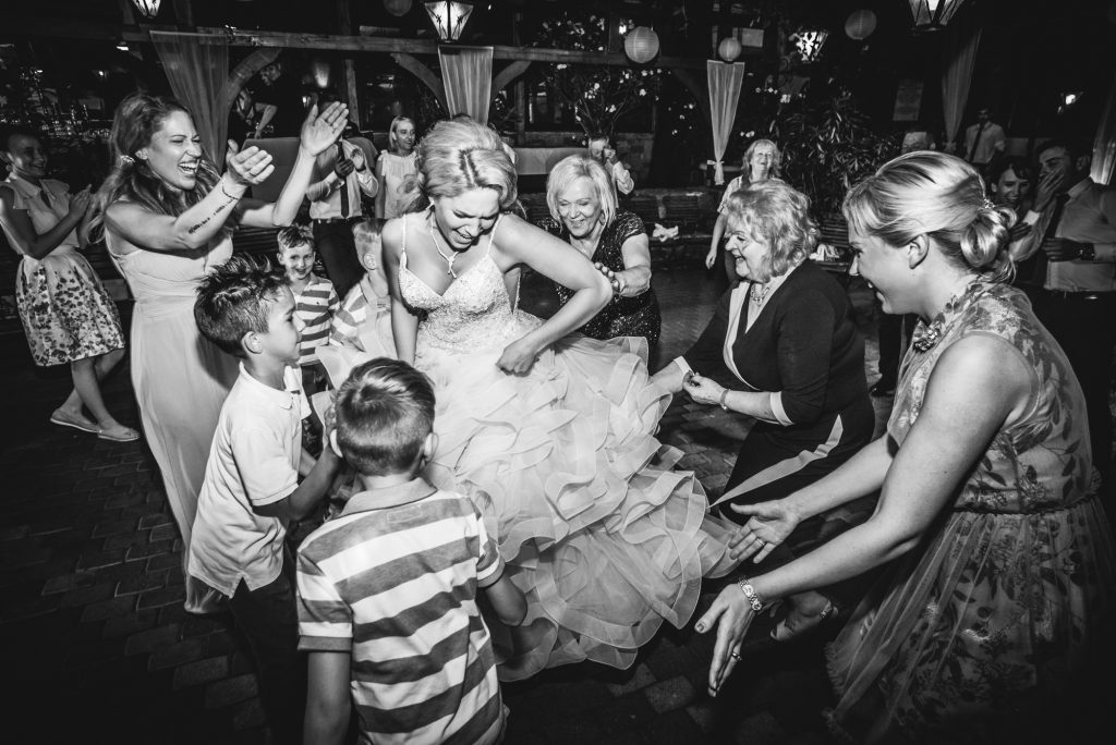 Bride surrounded by guests dancing energetically during evening wedding celebration.