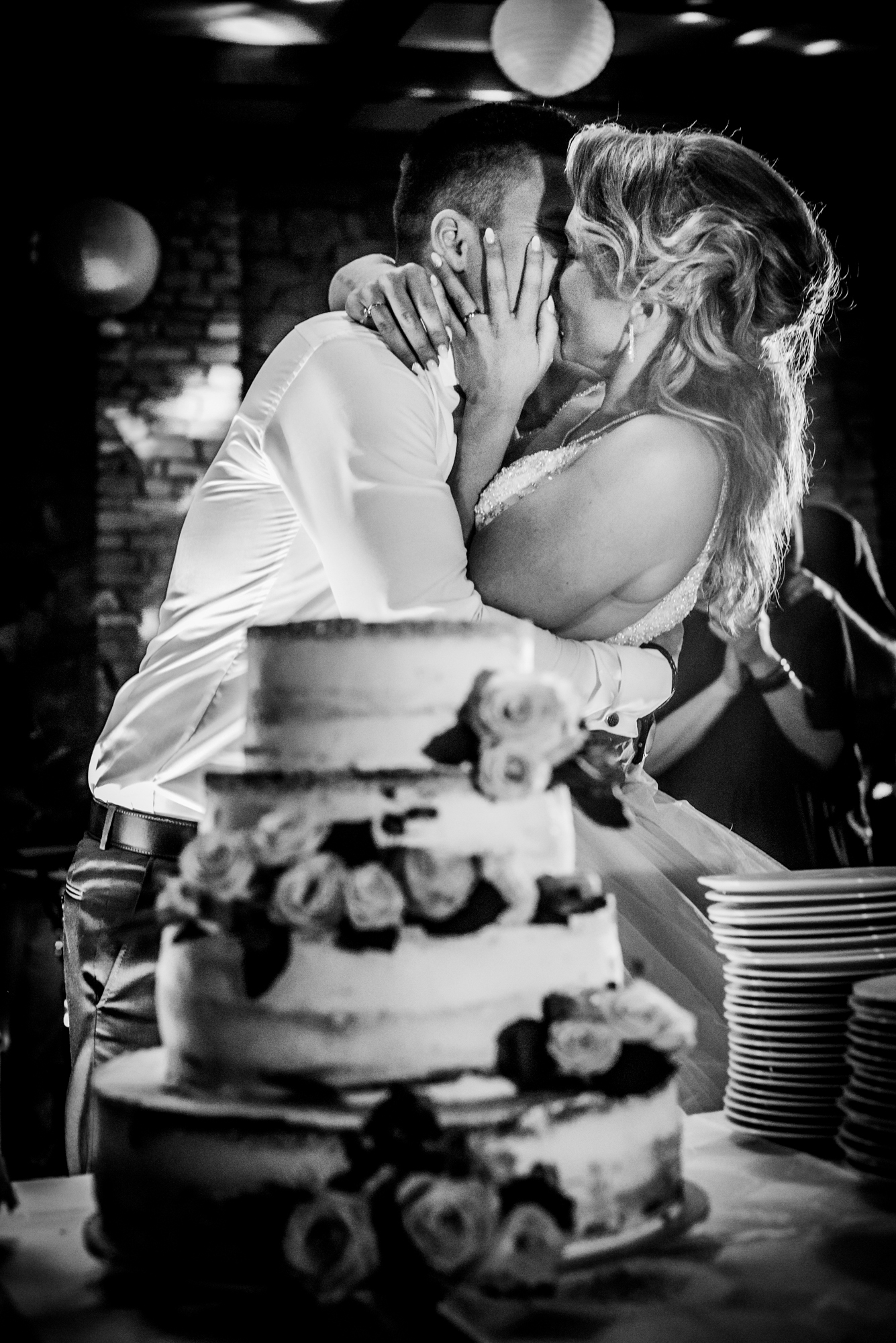 Bride and groom kissing behind wedding cake during evening celebration.