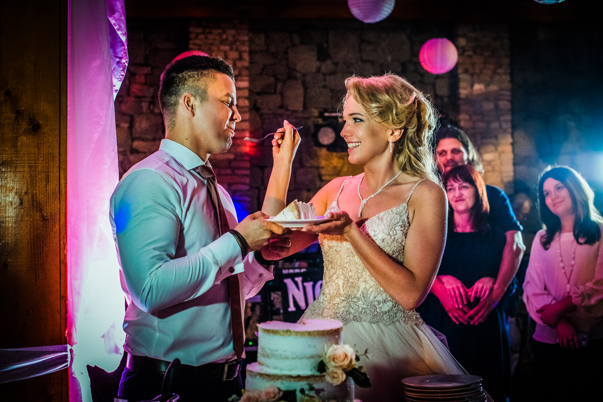 Bride feeding groom cake during playful wedding cake cutting moment.