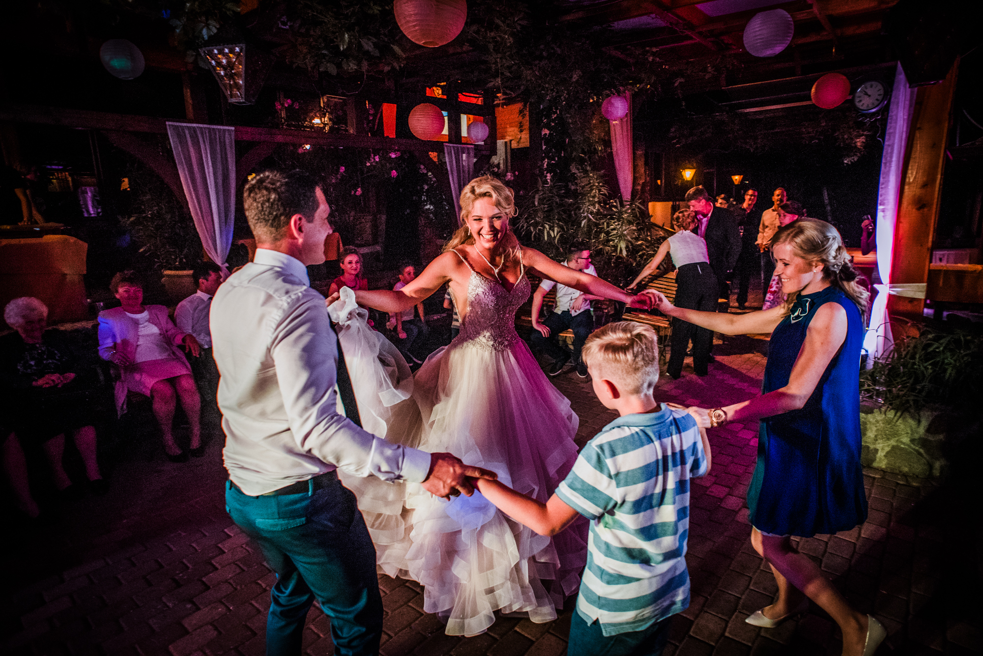 Bride dancing in circle with guests during lively evening wedding reception.