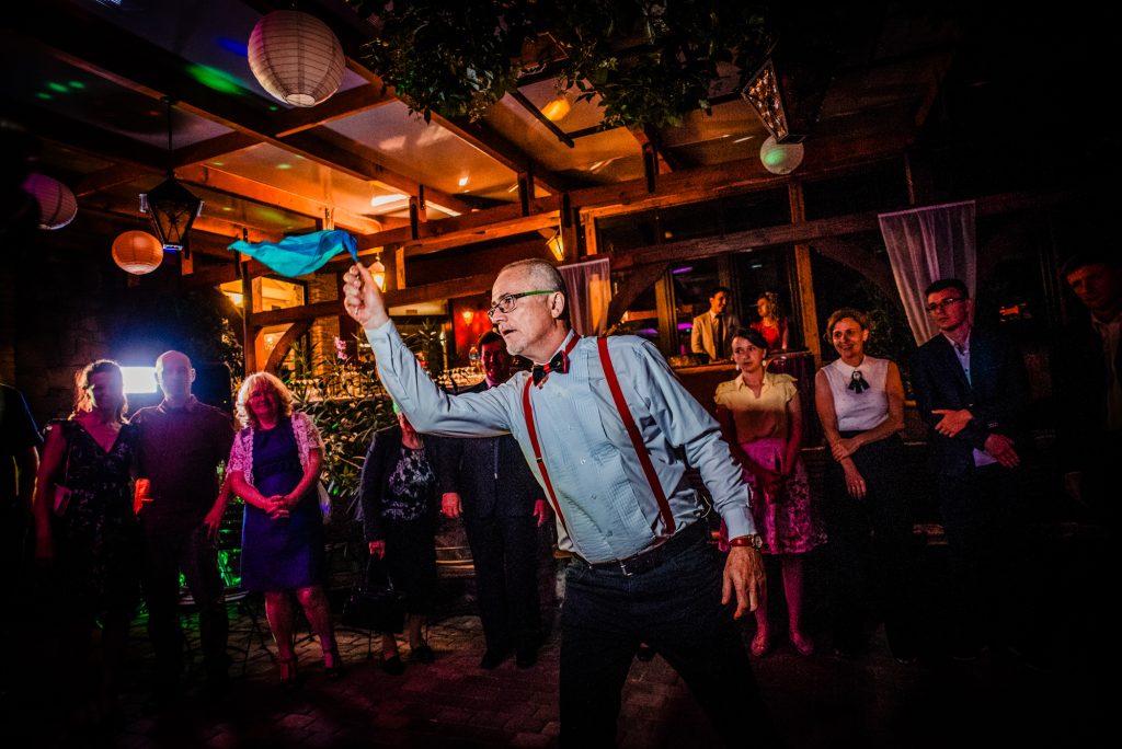 MC in red braces waving a scarf above his head while leading the crowd on the dance floor at the Nagyvillám Restaurant wedding party.