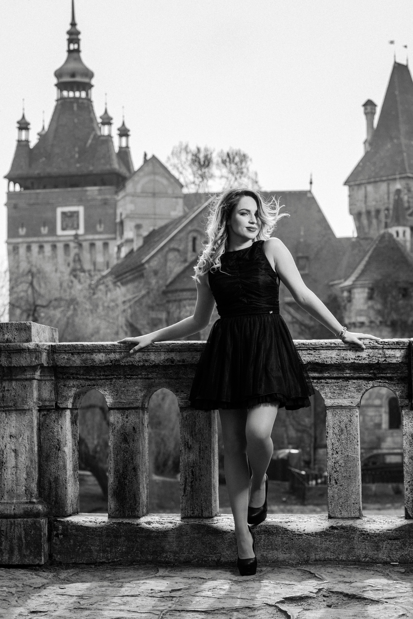 Black and white portrait on stone balcony with historic Budapest backdrop.