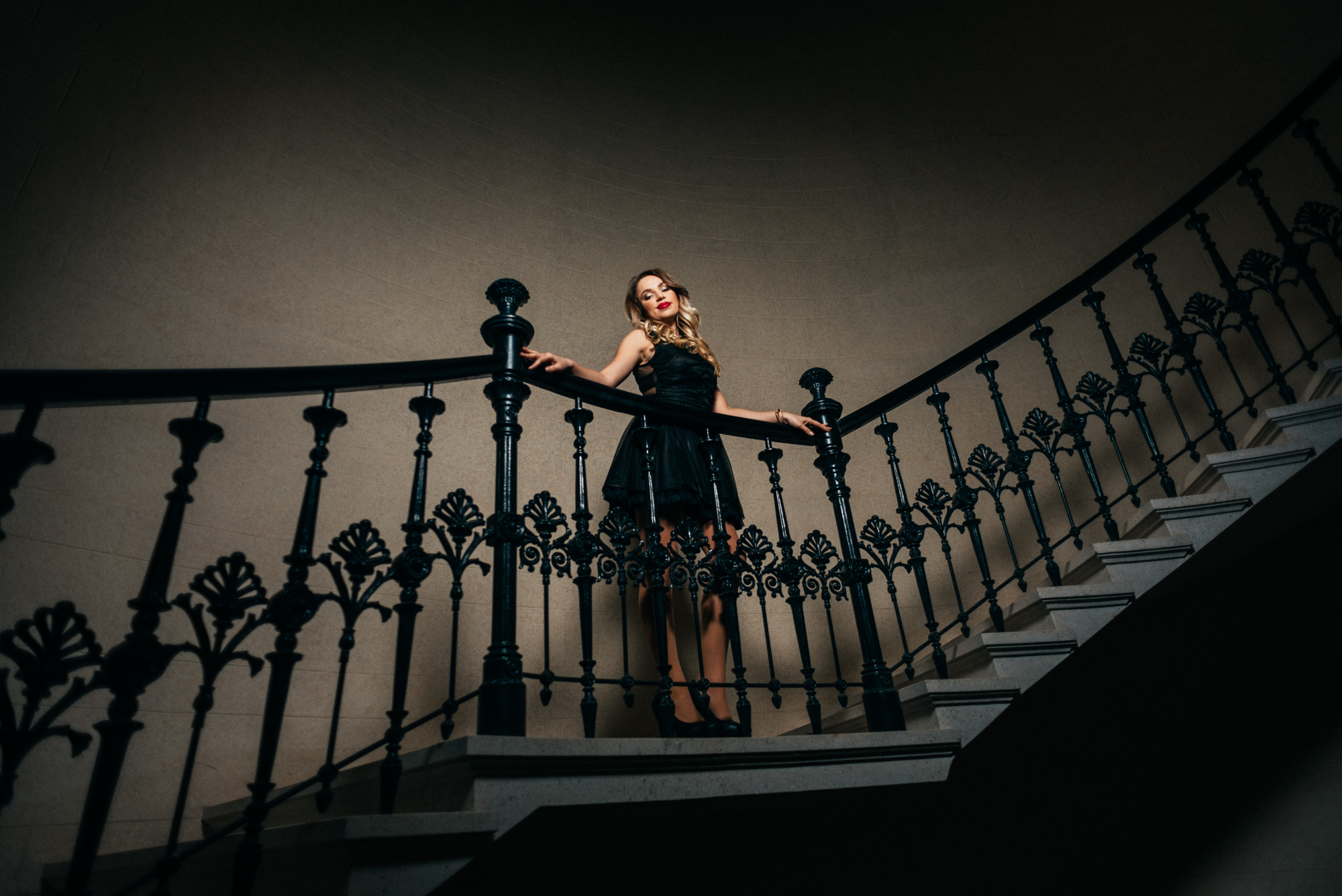 Woman posing on elegant curved staircase with black iron railings indoors.