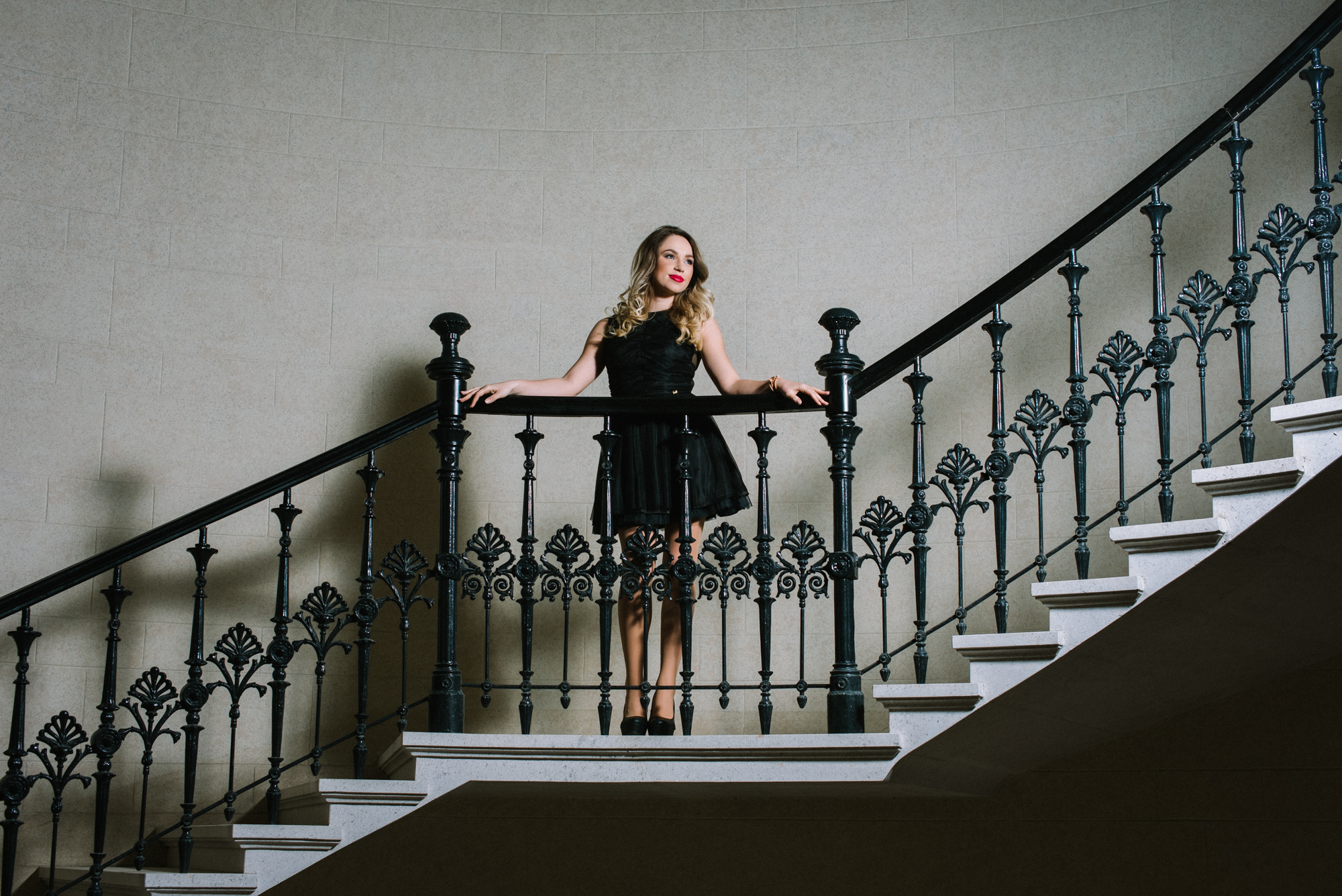 Wide shot of staircase with ornate railing and confident standing pose.