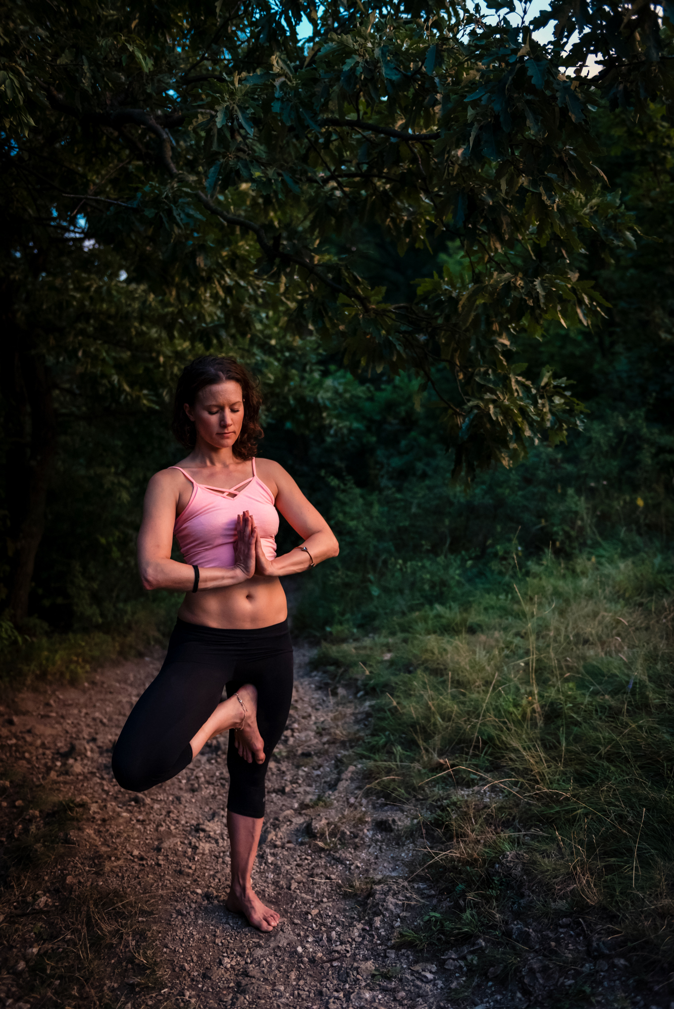 Woman in pink sports top practising yoga on a rocky forest trail at sunset in Budapest.