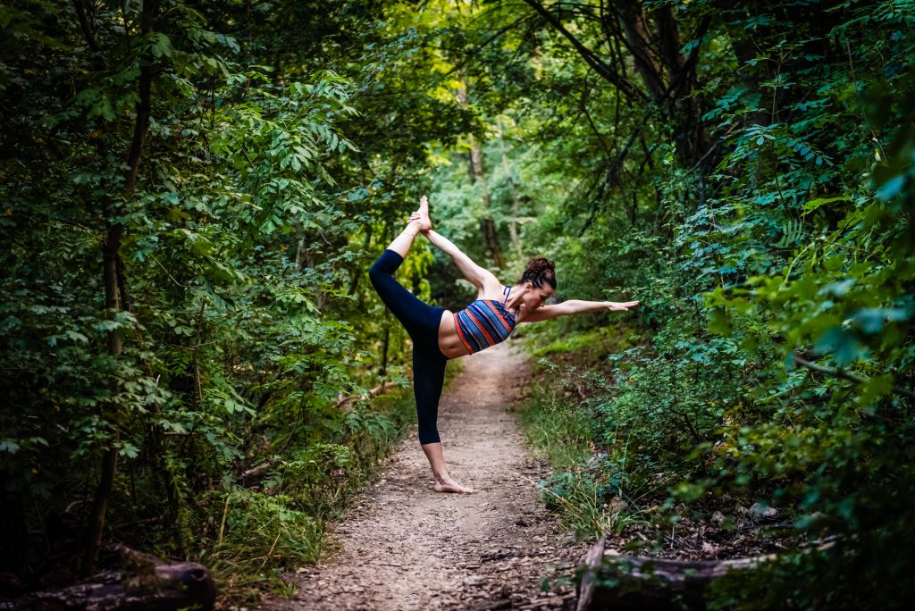 Yoga teacher performing dancer pose on a woodland trail at Three Border Mountain in Budapest.