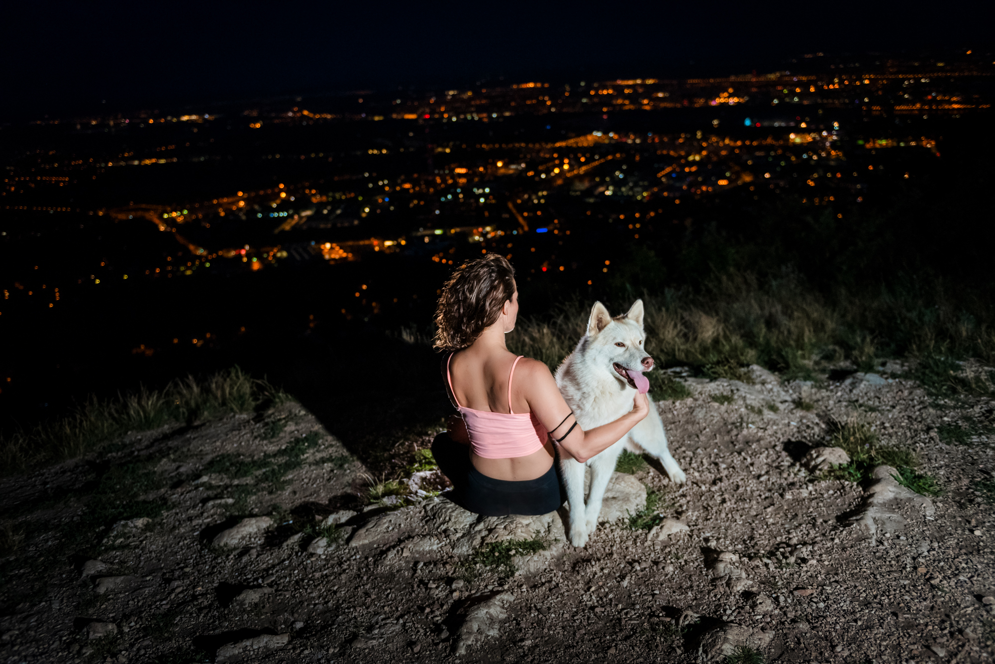 Yoga teacher sitting beside a white husky overlooking Budapest during a nighttime wellness photoshoot.