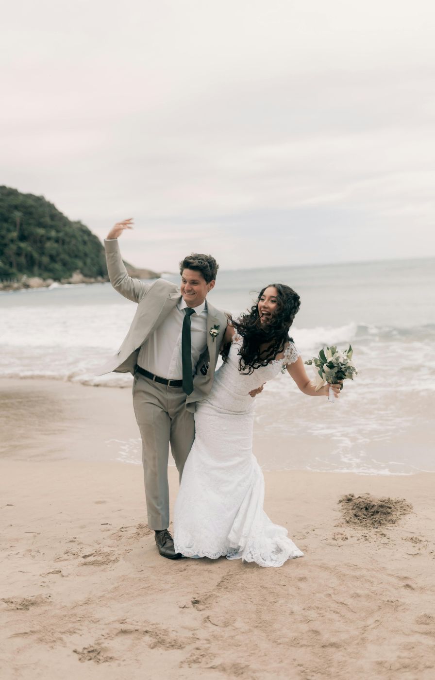 Newlyweds laughing and playing on the beach, a fun and carefree moment.