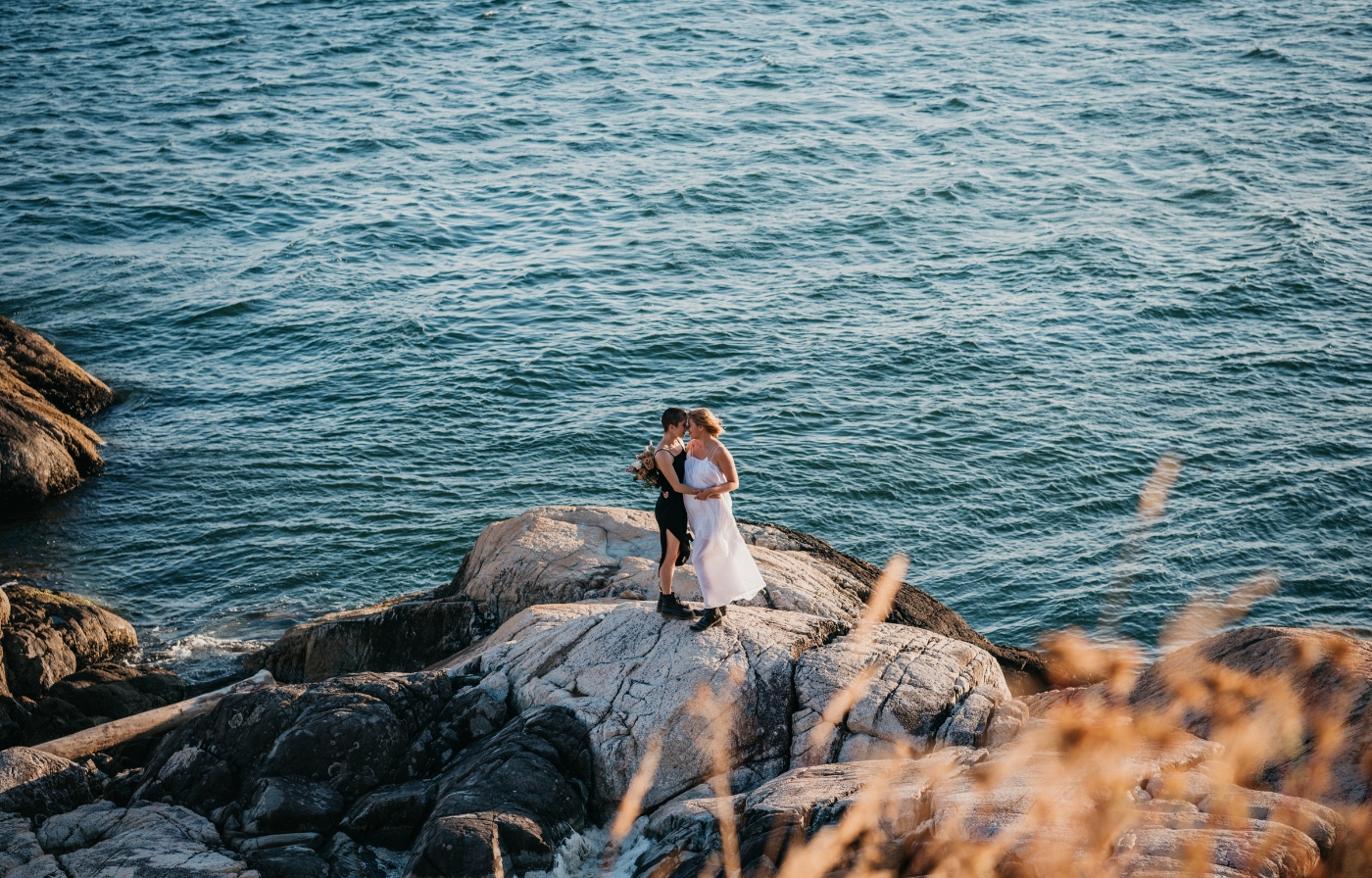 Two brides embracing their love on seaside rocks with the ocean behind them.