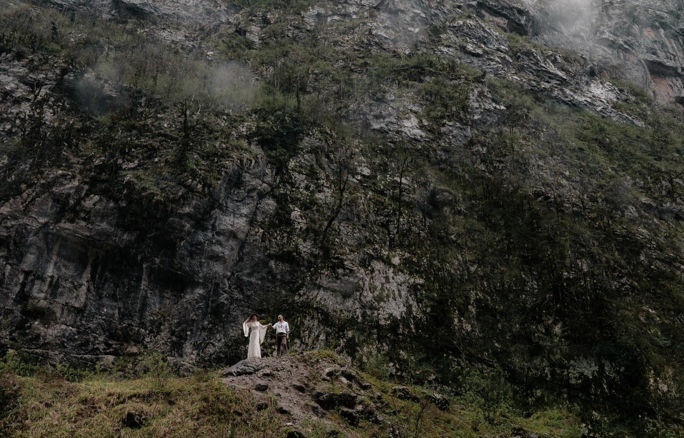 Couple standing beneath towering cliffs and misty rock walls, an adventurous setting for eloping in the UK.