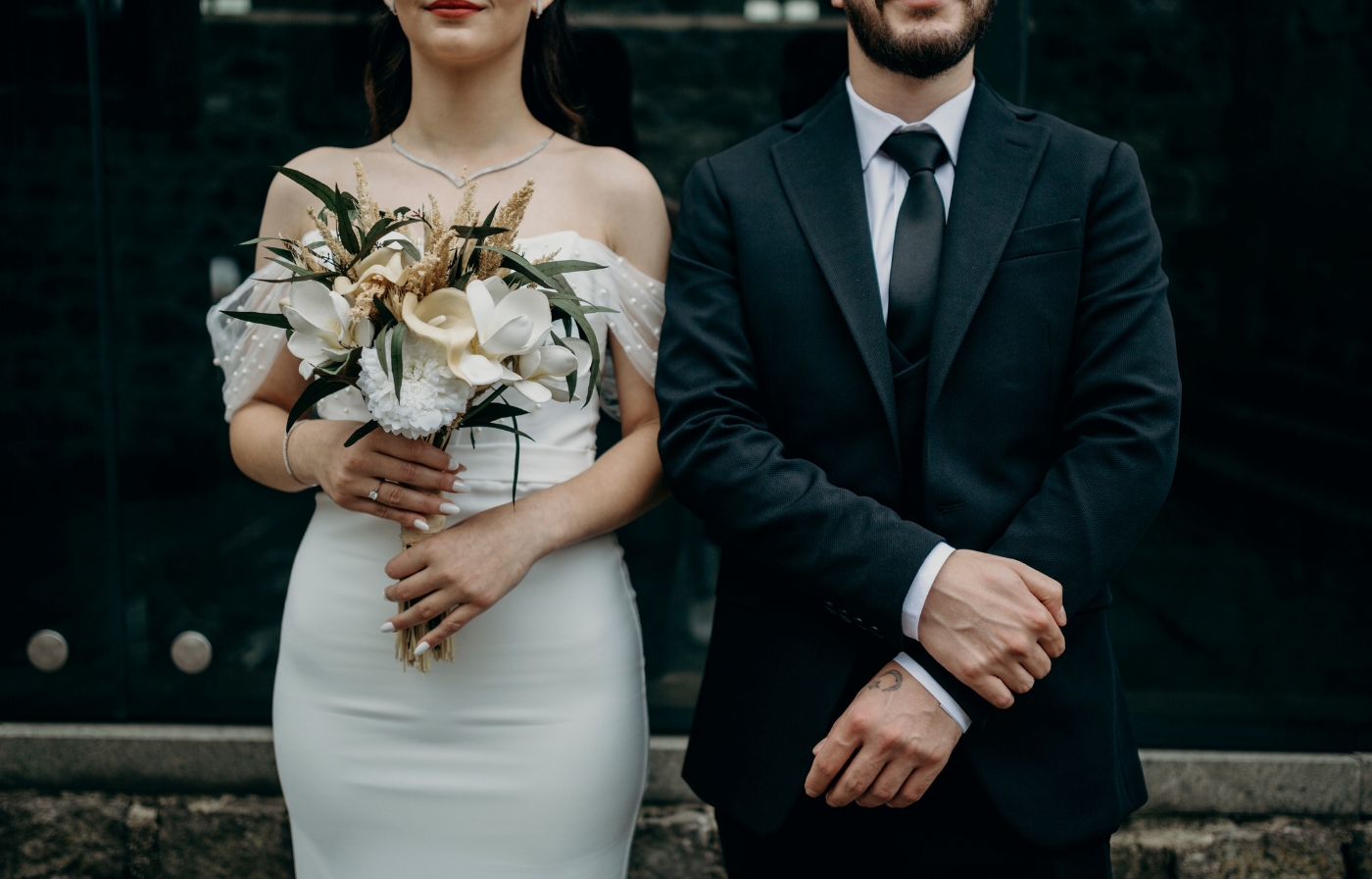 Close-up of a bride holding a white floral bouquet next to her groom.