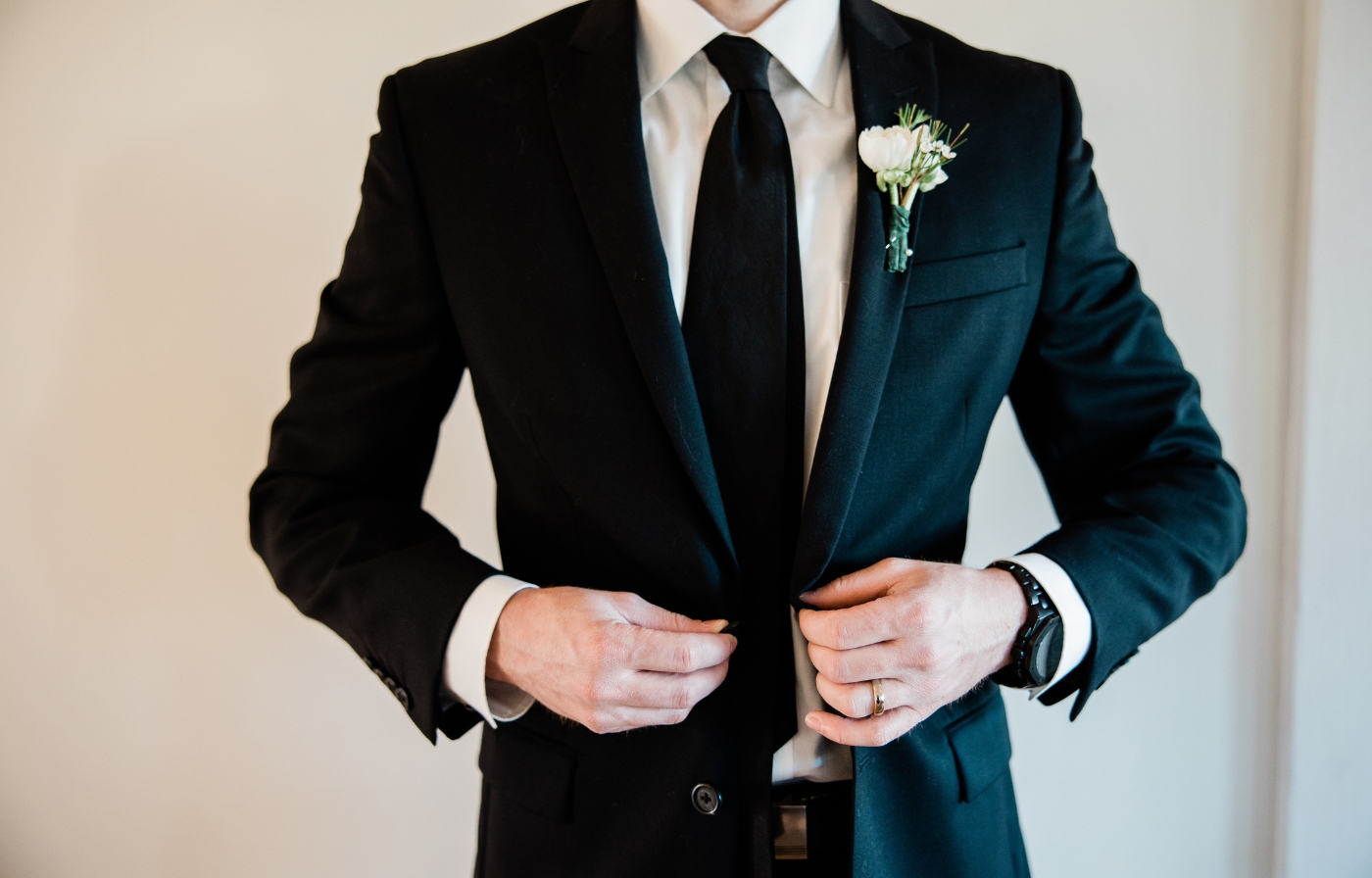Groom fastening his black suit jacket with boutonniere detail.