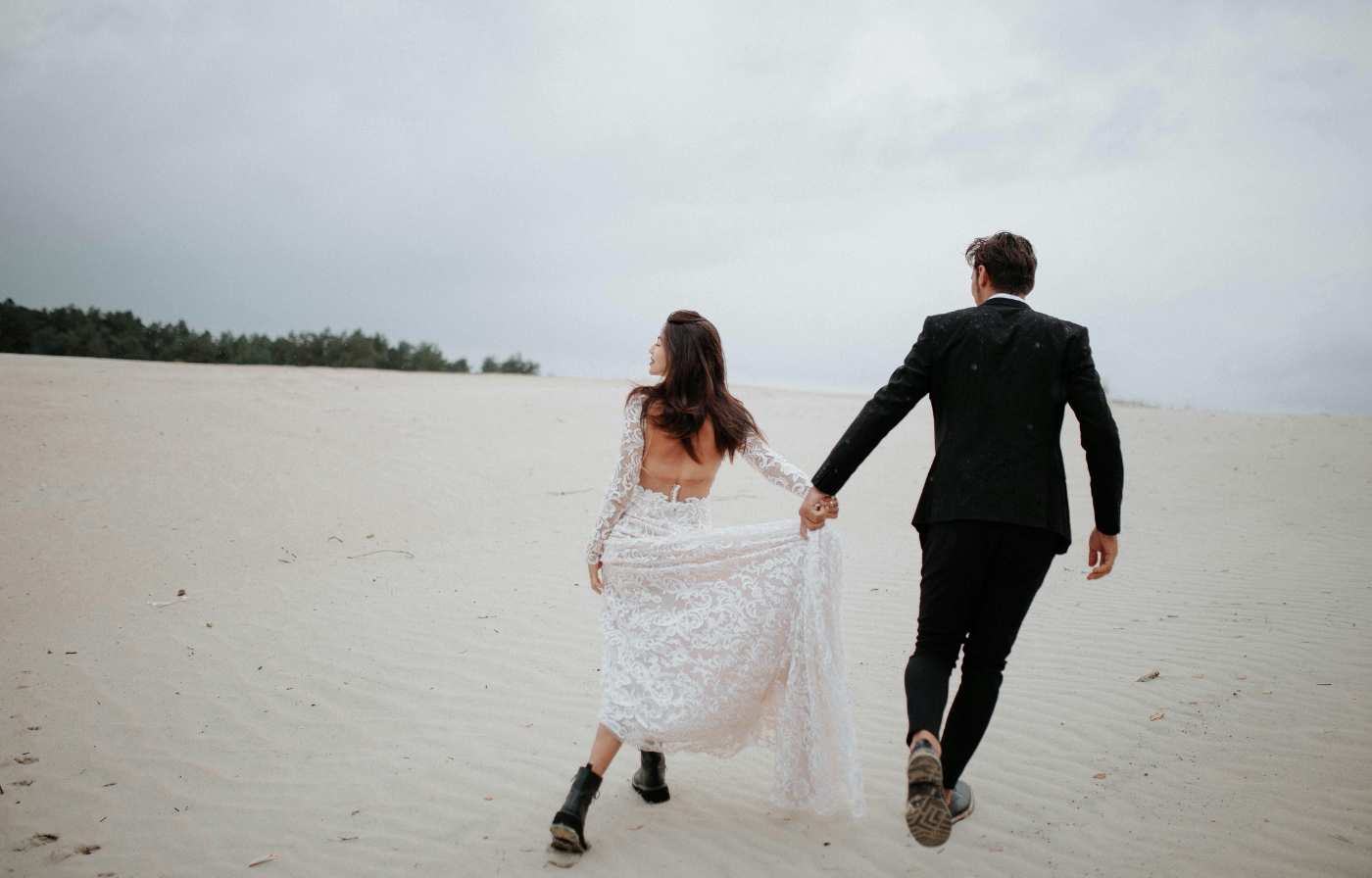 Newlyweds walking hand in hand across soft sand dunes, carefree adventure while eloping in the UK.
