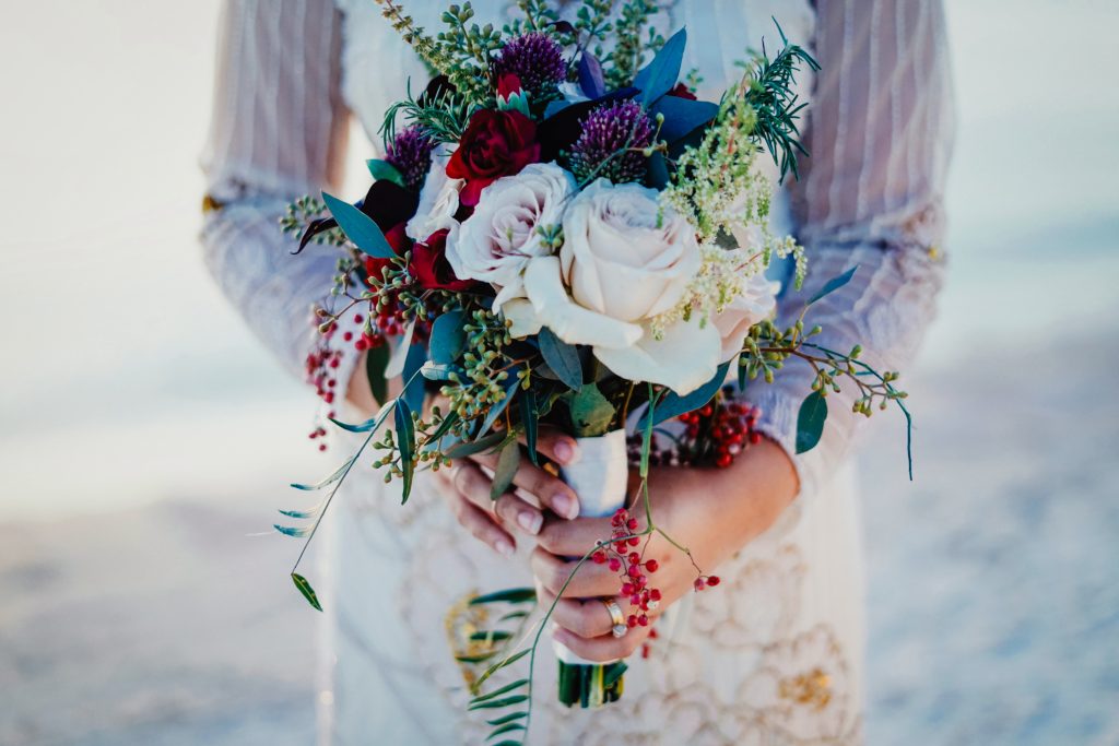 Winter bridal bouquet of roses, berries, and greenery in rich jewel tones.