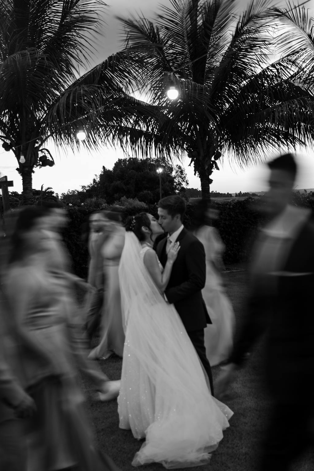 A romantic outdoor wedding captured in black and white, with a couple surrounded by blurred guests.