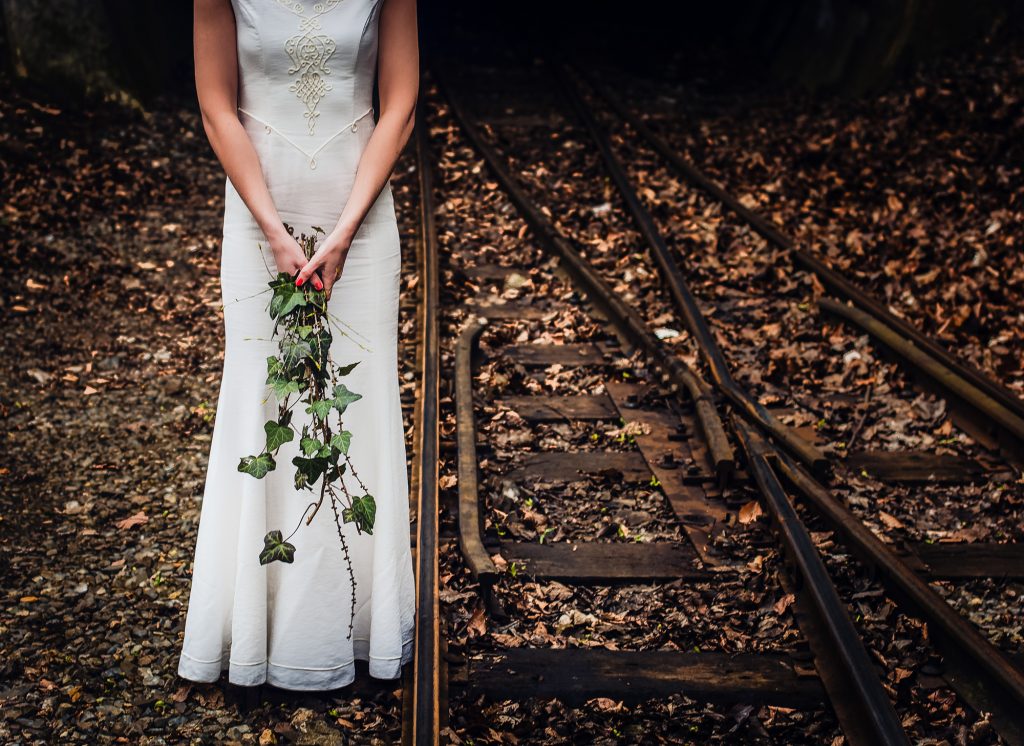 Unique bridal details of a bride holding ivy on old railway tracks covered in autumn leaves.