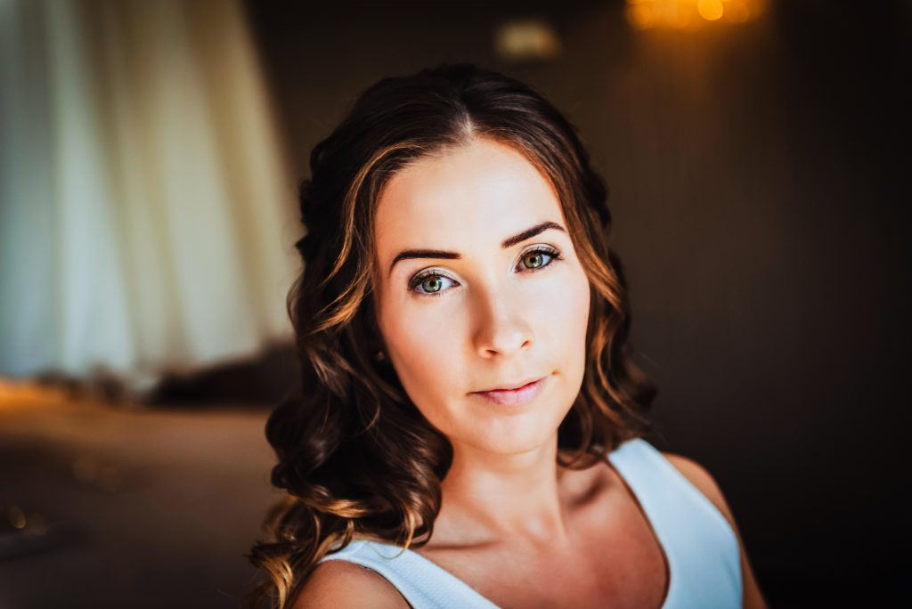 Soft bridal portrait of a bride with gentle curls looking into the camera in warm light.