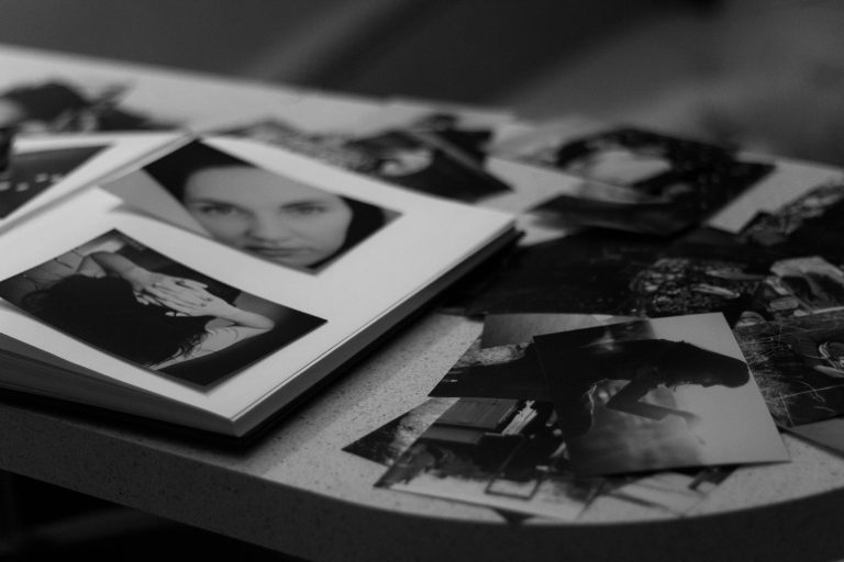 A collection of black and white photos in a photo album scattered on a table, featuring portraits and artistic compositions.
