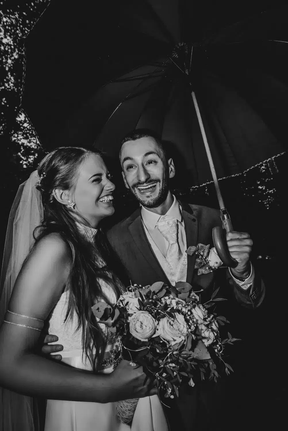 Joyful couple laughing under umbrella in the rain captured with candid wedding photography in Bristol