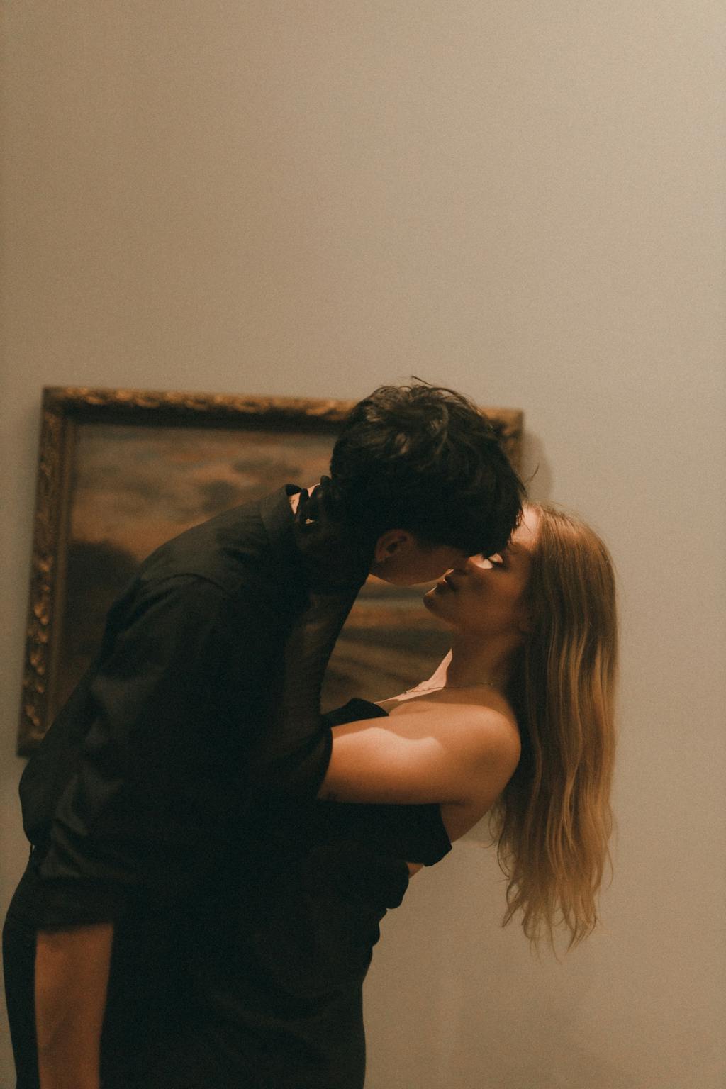 Intimate portrait of a couple kissing in an art gallery, exuding a warm and romantic atmosphere.