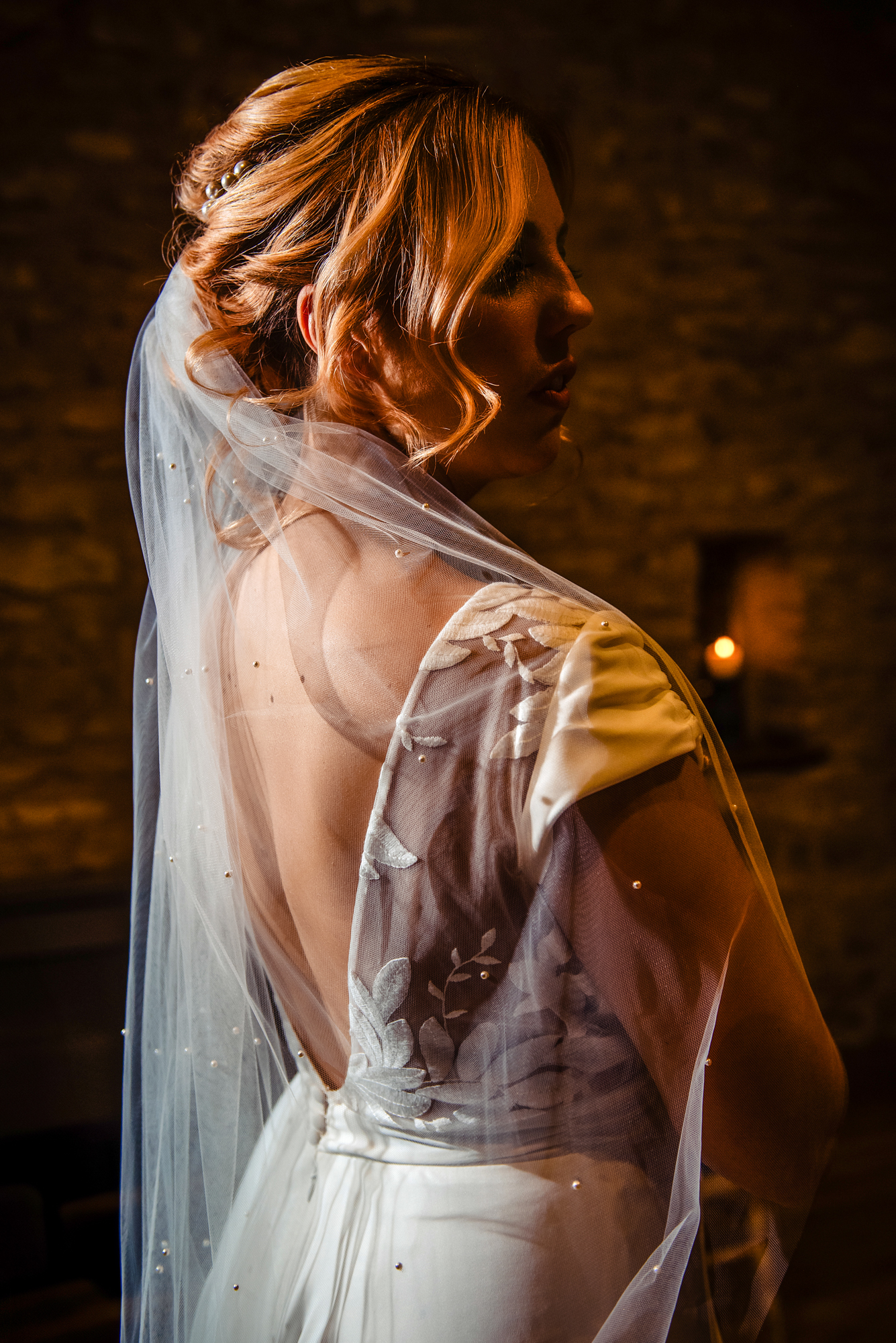 Bride’s pearl-dotted veil falling over her shoulder in warm candlelit shadows.