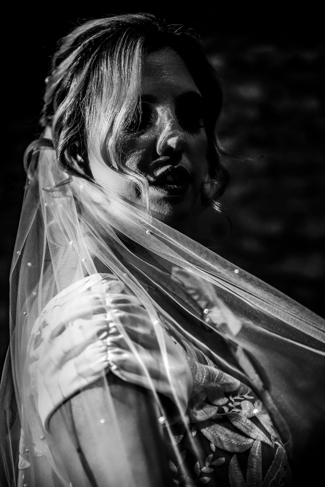 Dramatic shadow across the bride’s face as her veil moves through low light.