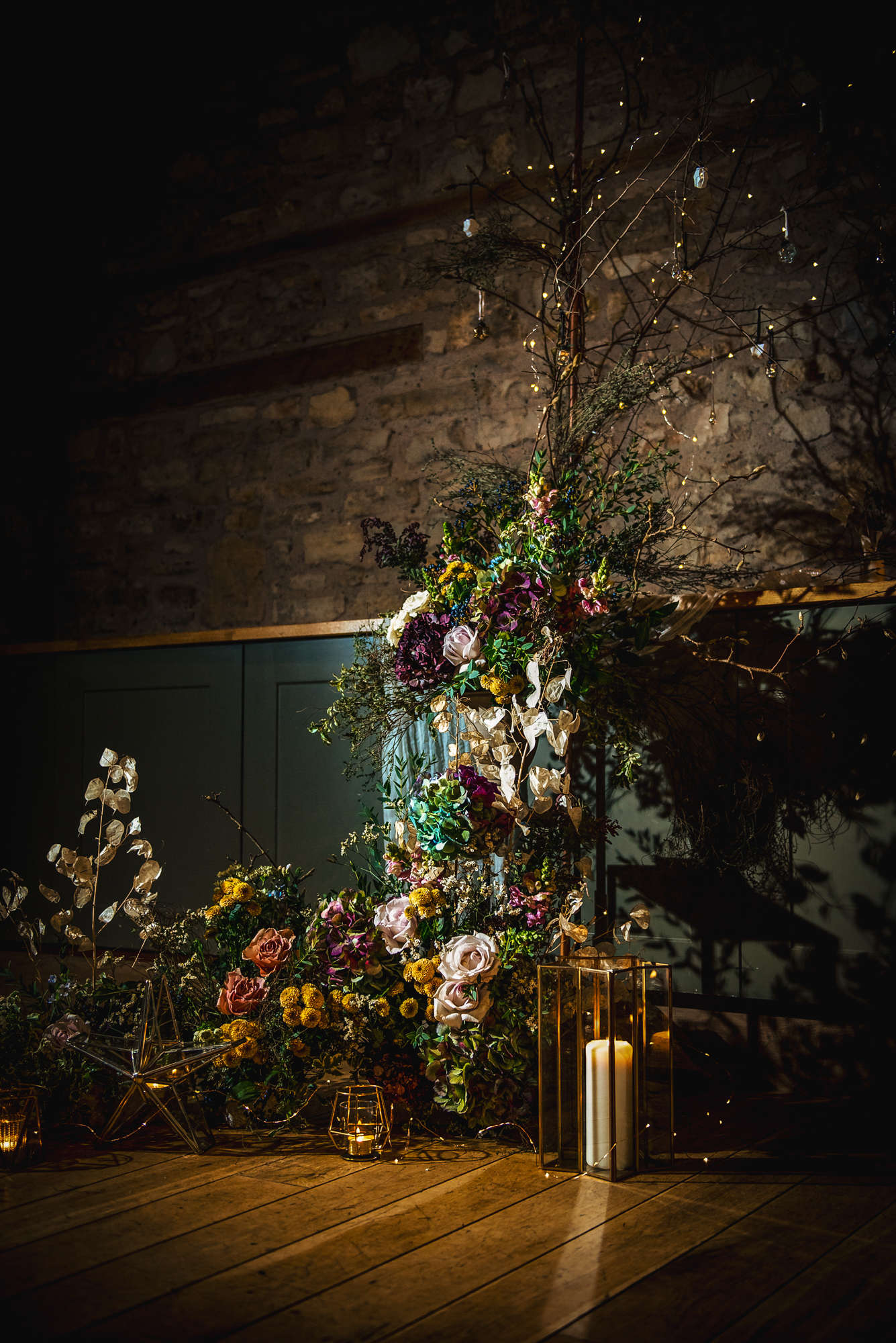 Tall floral installation with pastel blooms, dried botanicals, and soft lantern light.