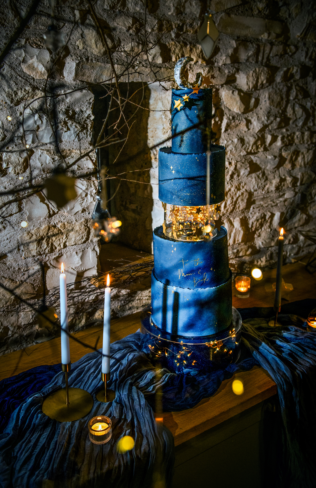 Blue galaxy-inspired wedding cake surrounded by hanging ornaments and candlelit décor.