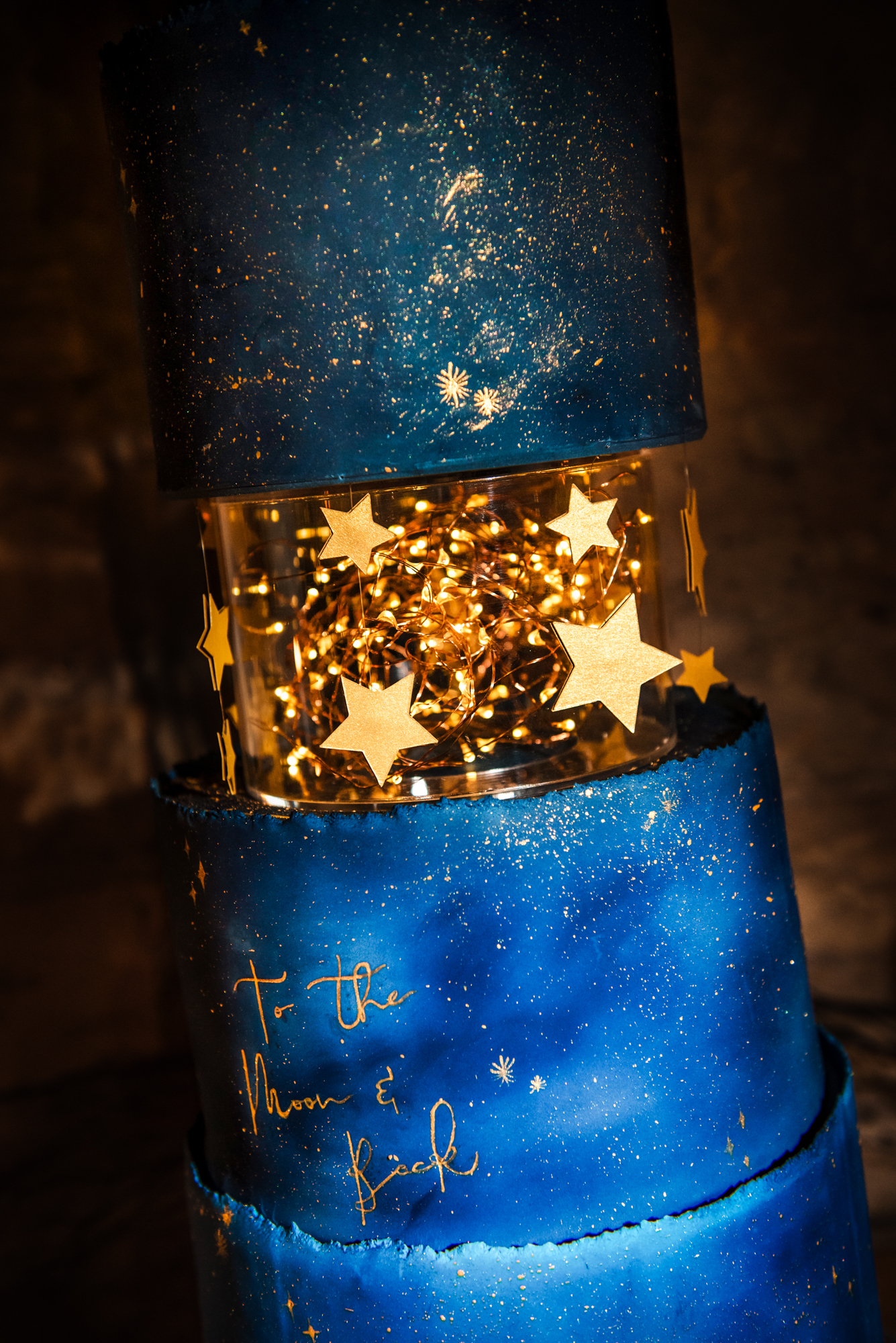 Close-up of glowing fairy lights and gold stars inside the transparent tier of the wedding cake.