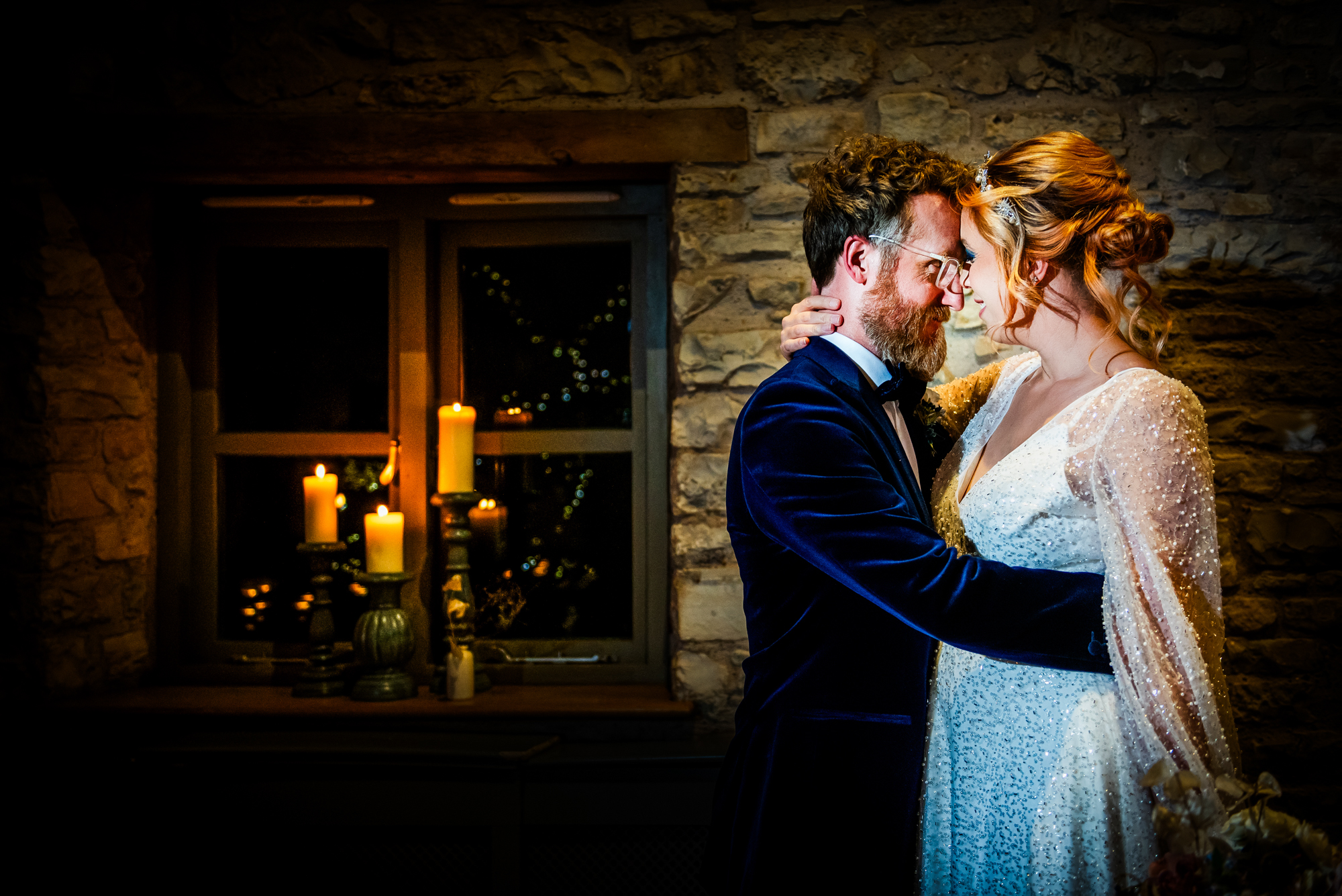 Couple embracing gently beside a window filled with warm candlelight during the winter wedding editorial.