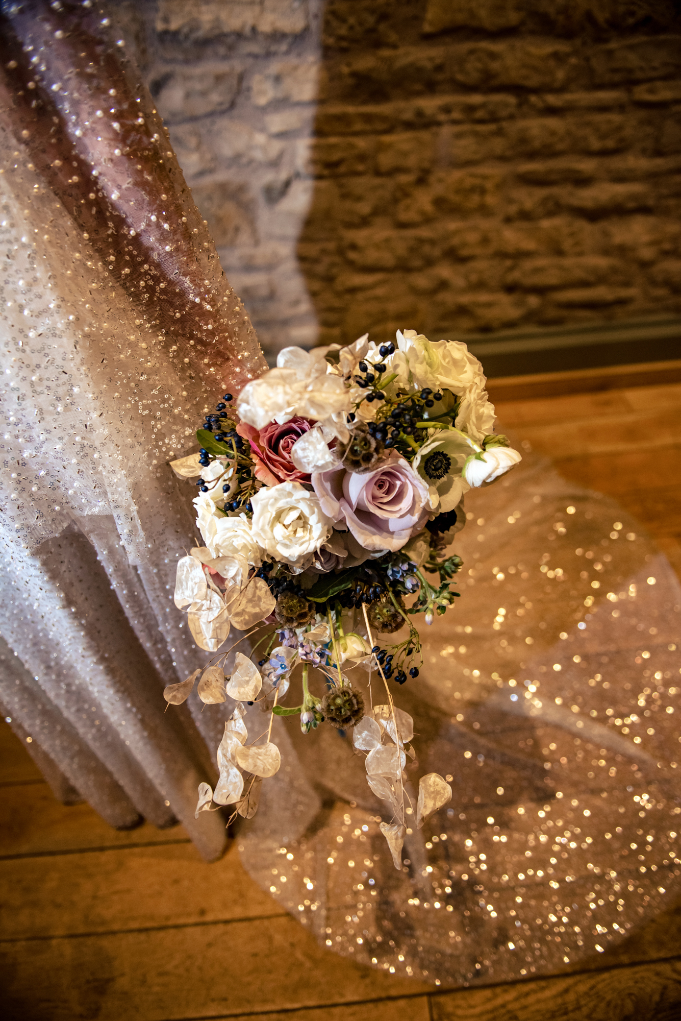 Winter bridal bouquet held beside the bride’s sparkling gown with soft light catching the sequins.