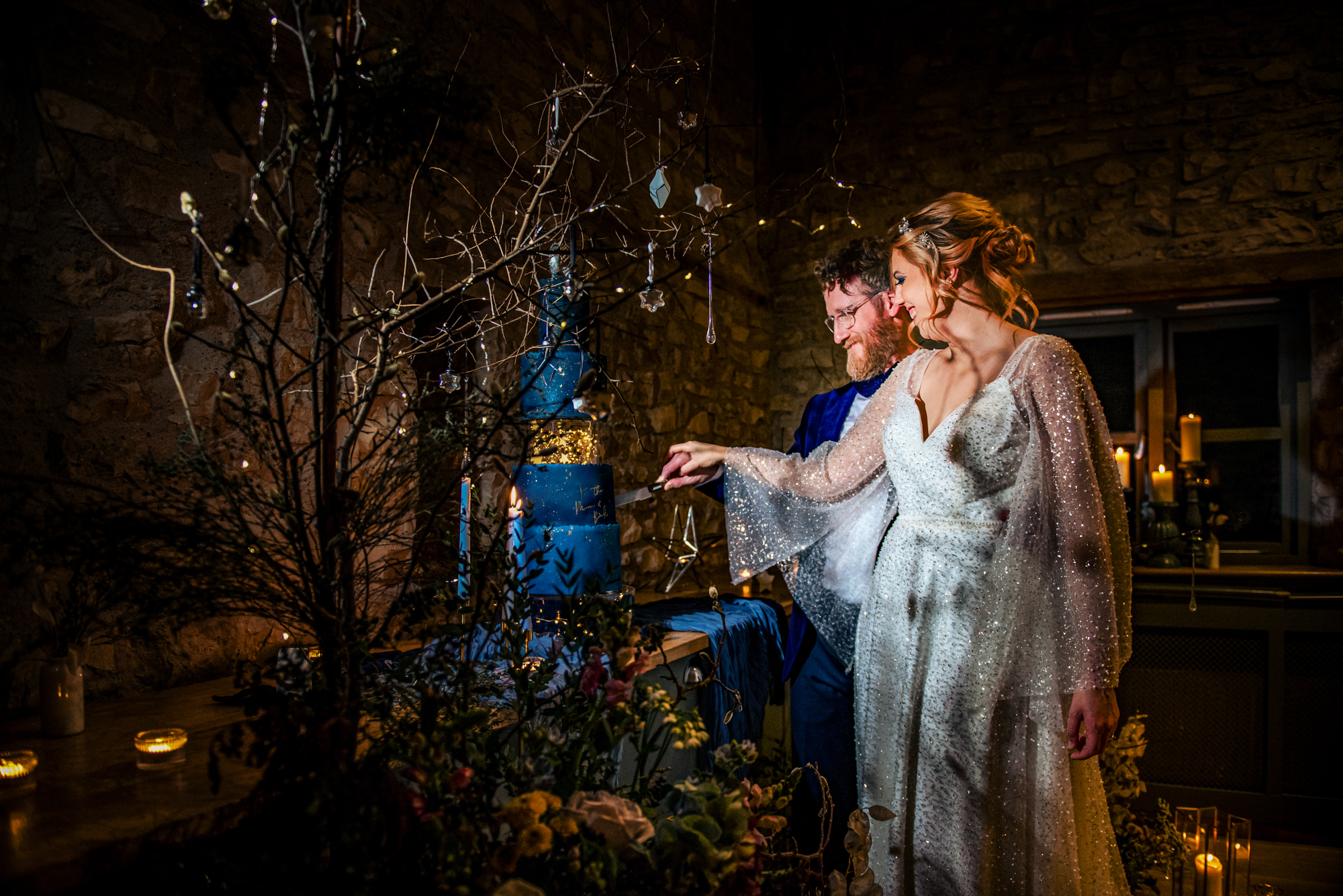Couple cutting their celestial blue wedding cake surrounded by candlelight and hanging star decorations.