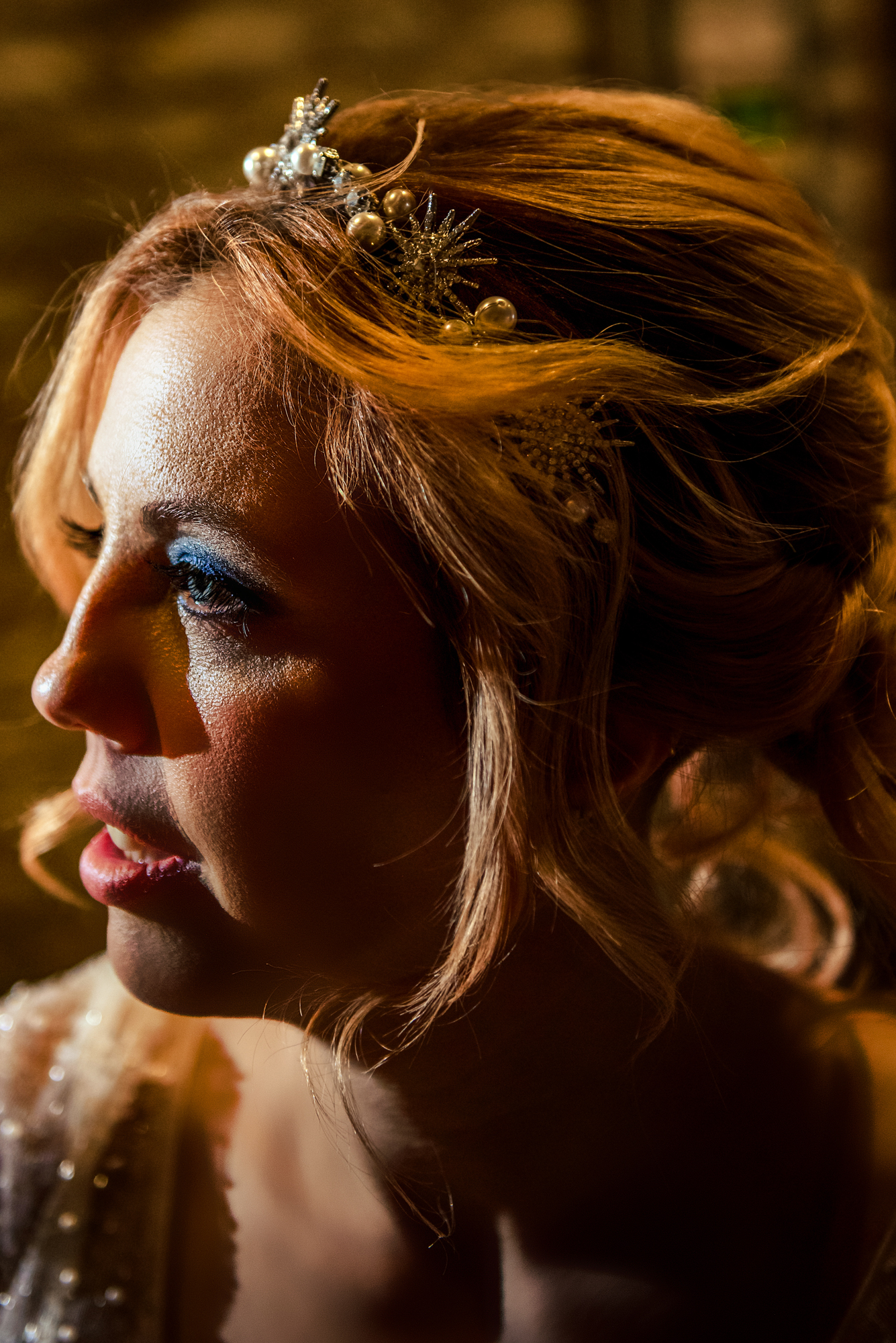 Warm side-lit bridal portrait highlighting blue eyeshadow, soft waves, and the celestial hairpiece.