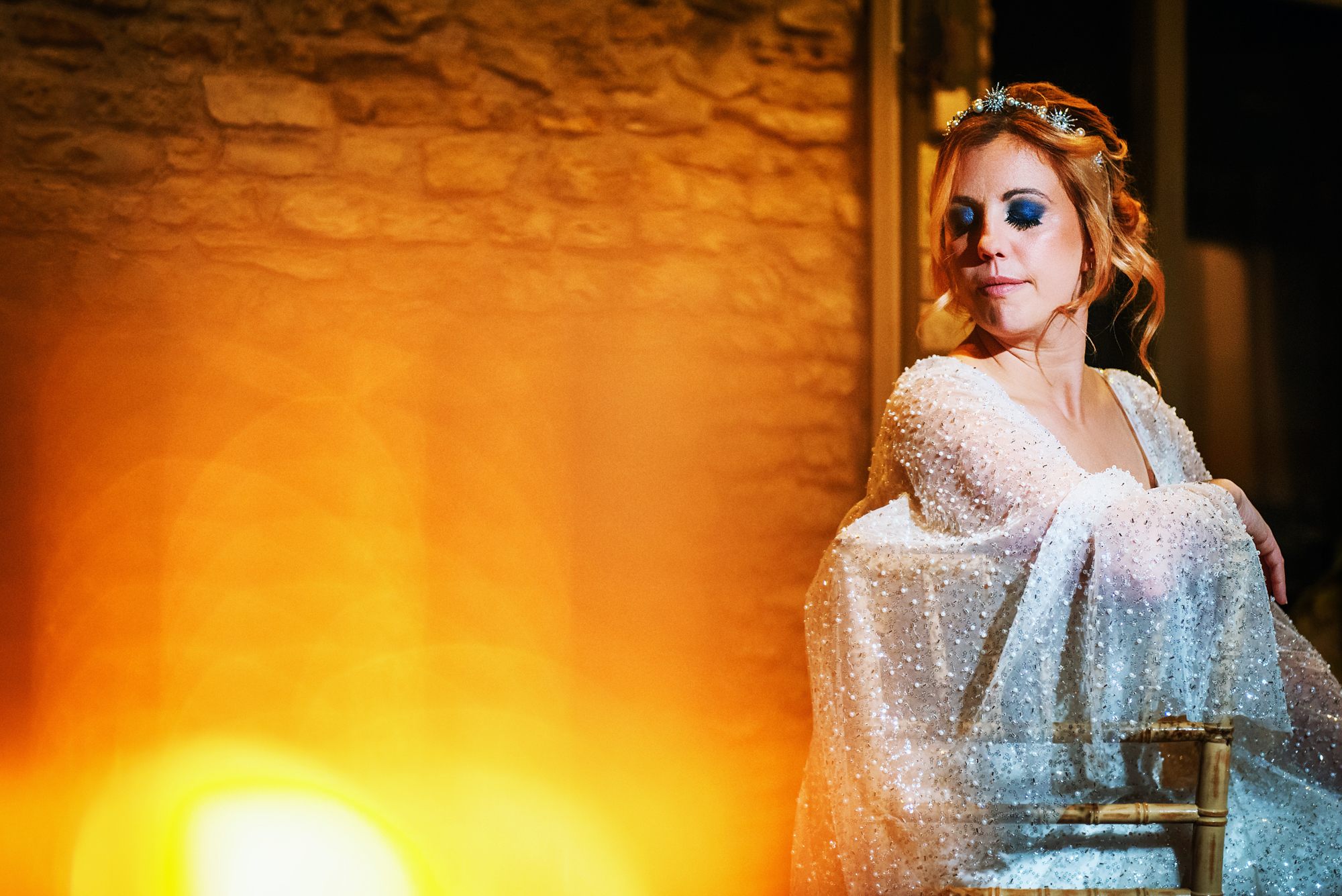 Bride seated with her eyes closed while golden lens flare glows across the frame.