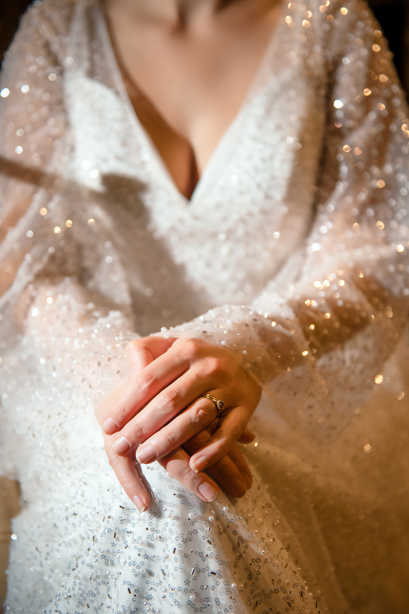 Bride’s hands resting gently on her sequinned gown with her engagement ring catching the light.