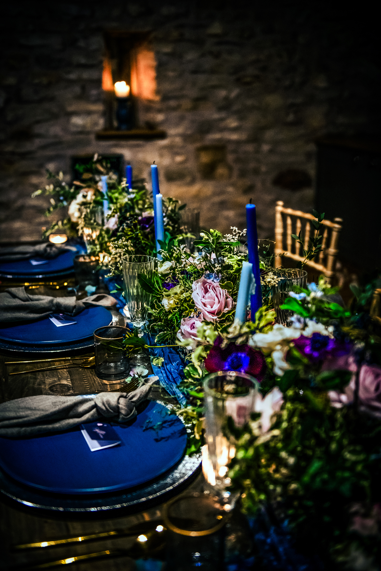 Celestial-themed tablescape with blue candles, floral arrangements, and deep blue plates set for dinner.