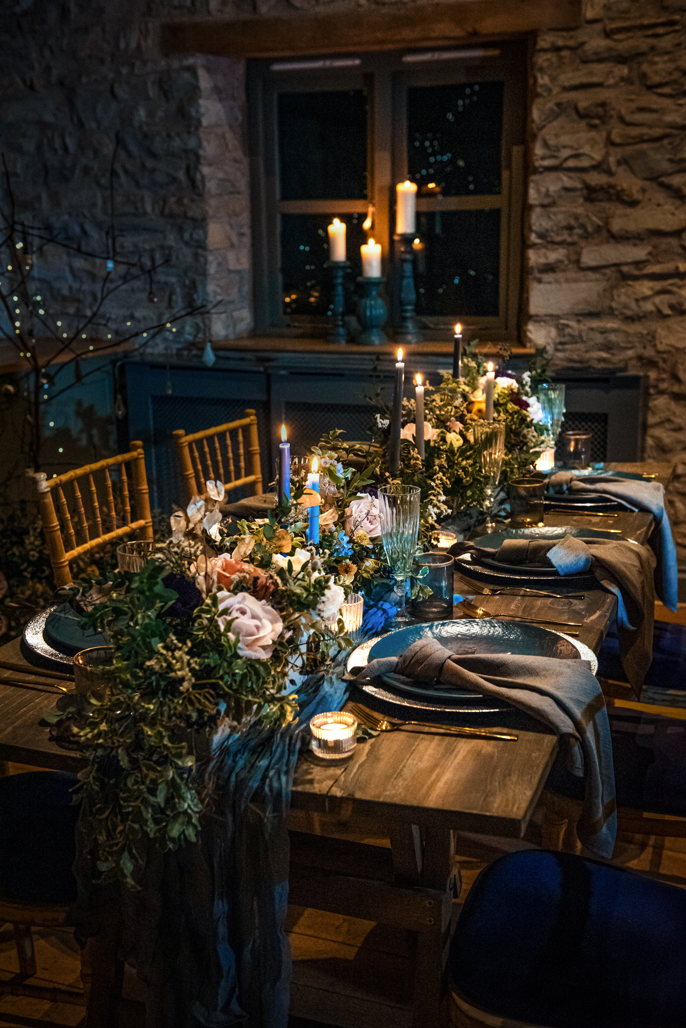 Candlelit tablescape decorated with blue candles, lush winter florals, and deep blue plates at Folly Farm.